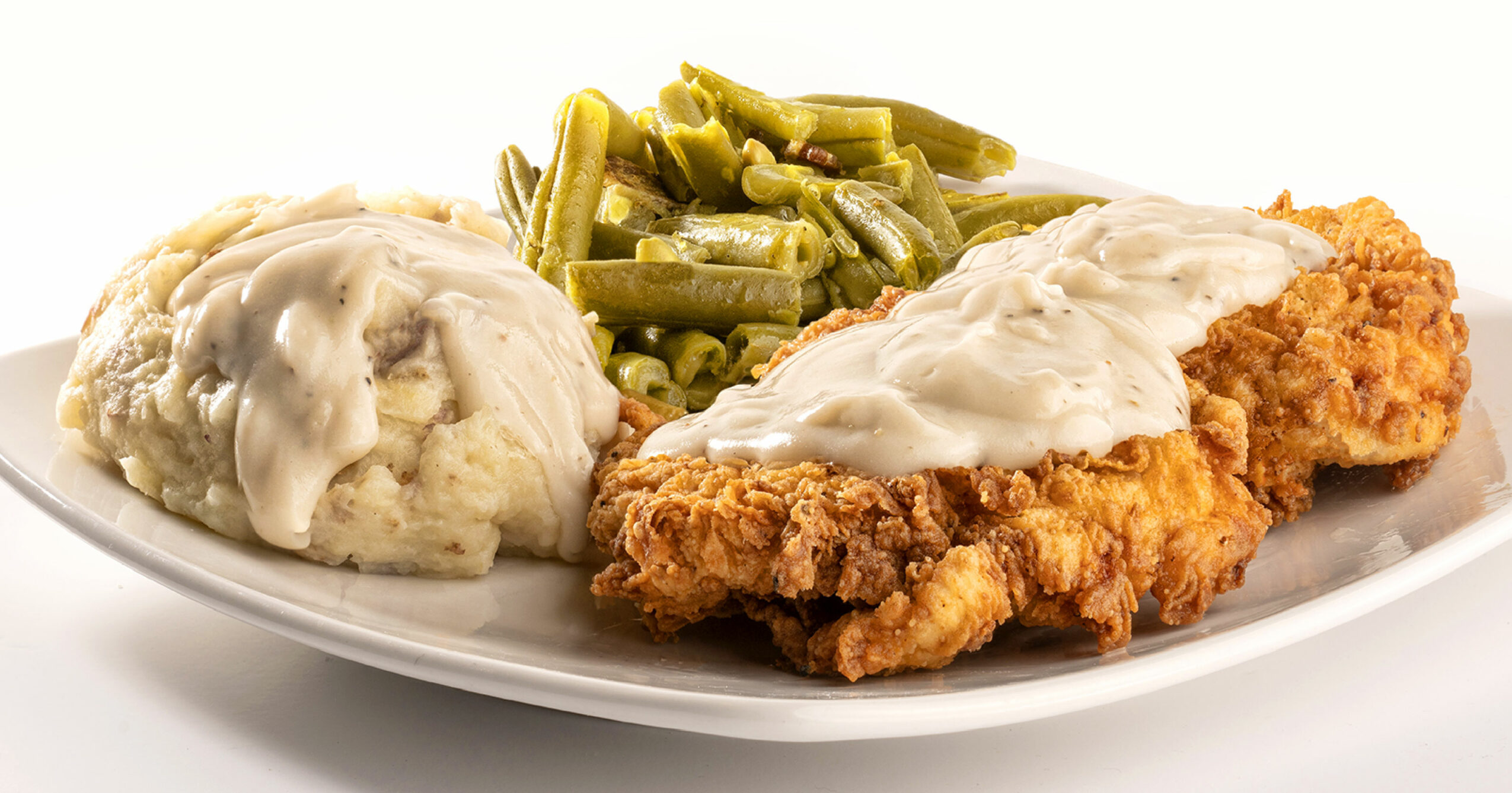Plate with mashed potatoes, green beans, and fried chicken with gravy, on a white background.