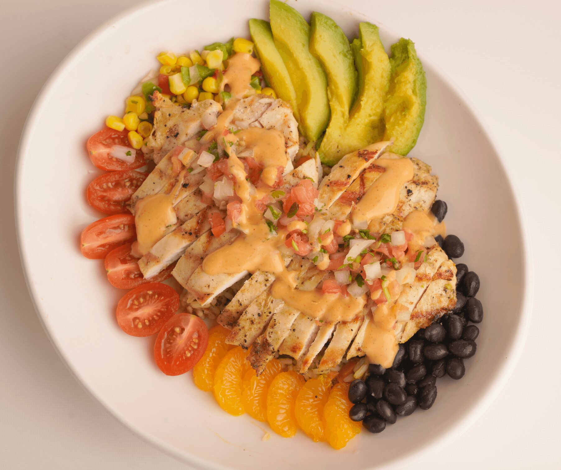 Sliced grilled chicken with cherry tomatoes, black beans, yellow and orange fruit slices, avocado slices, and corn on a white plate.