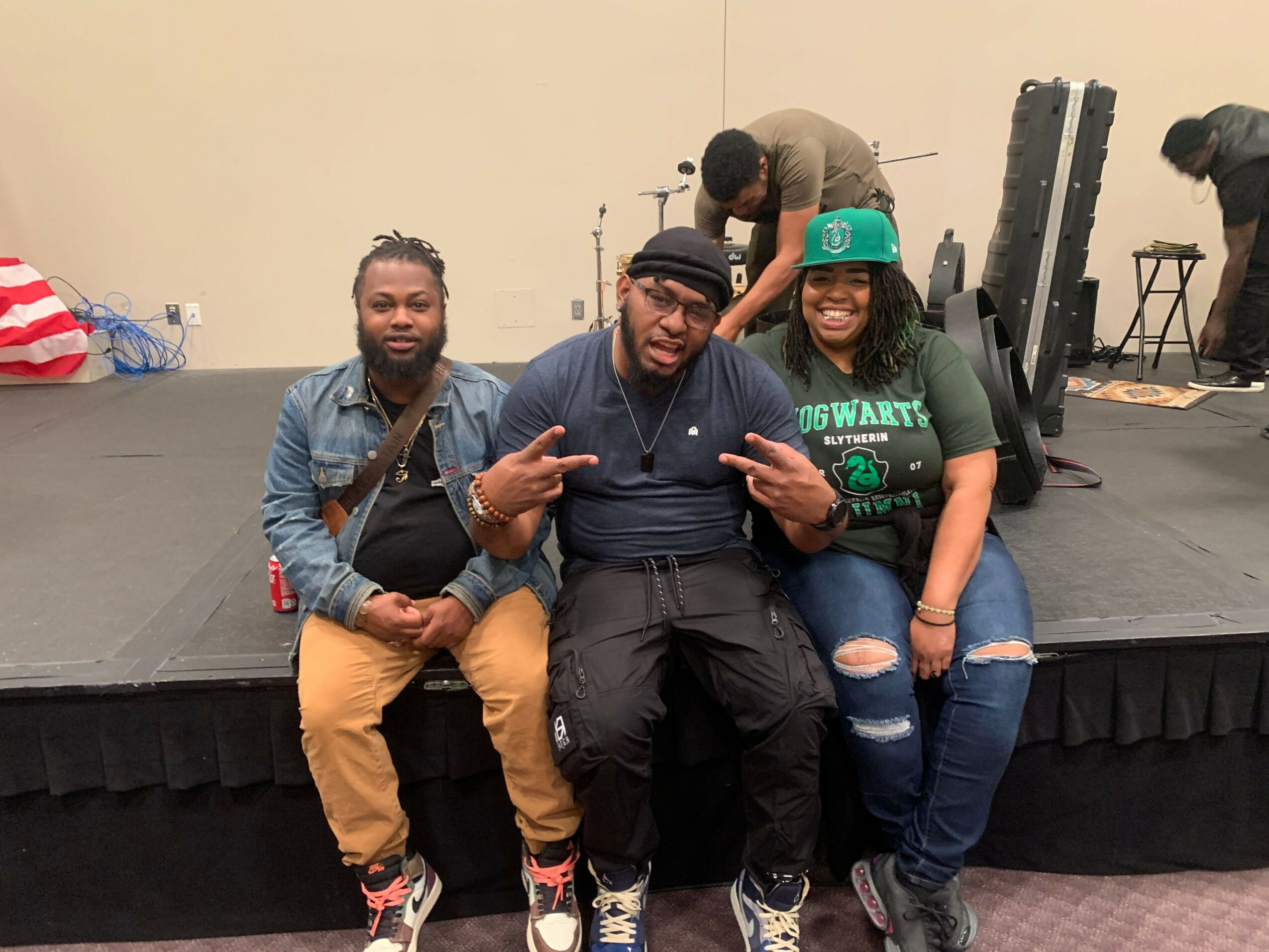 Three people sitting on a black couch, smiling, with a woman wearing a green cap, and a child in a yellow jacket.