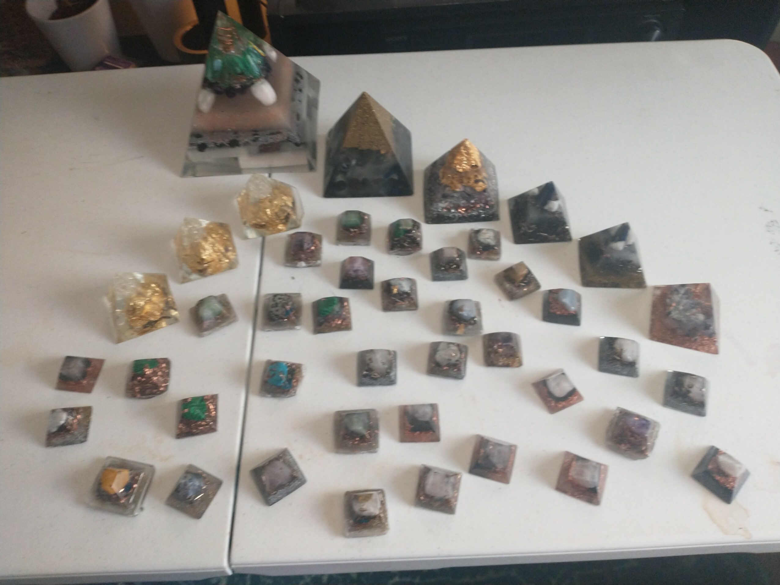 Collection of small mineral or gemstone specimens arranged on a white surface, with some larger pyramid-shaped stones at the back.