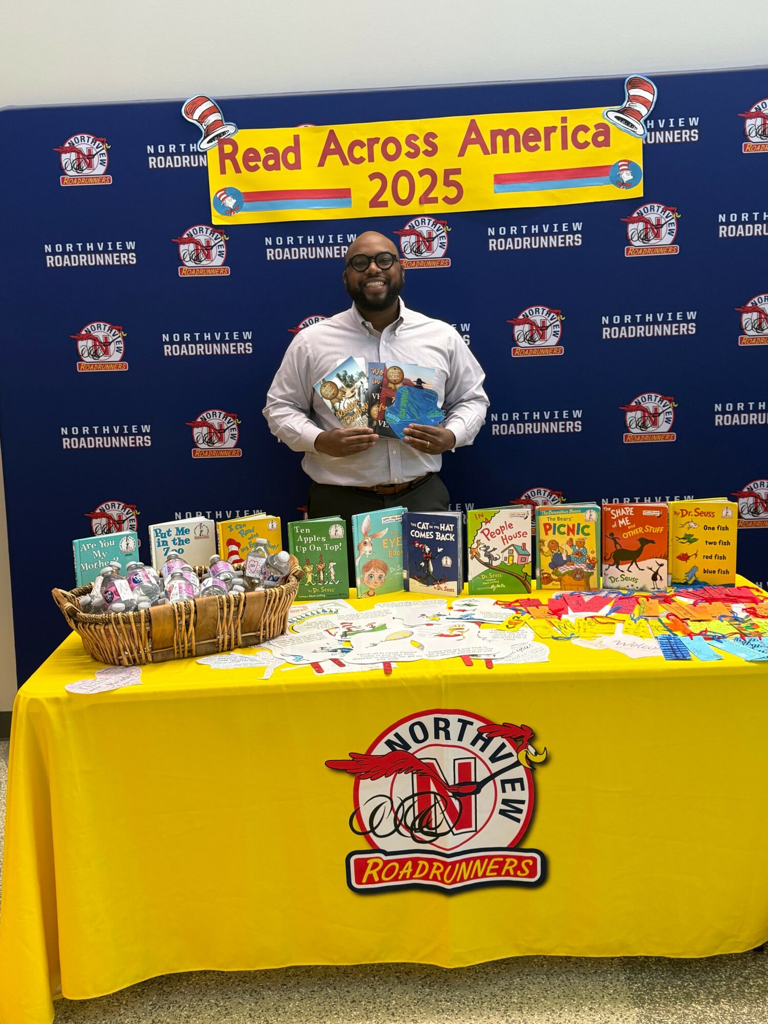Person standing behind a table with books and a Northview High School banner in the background.