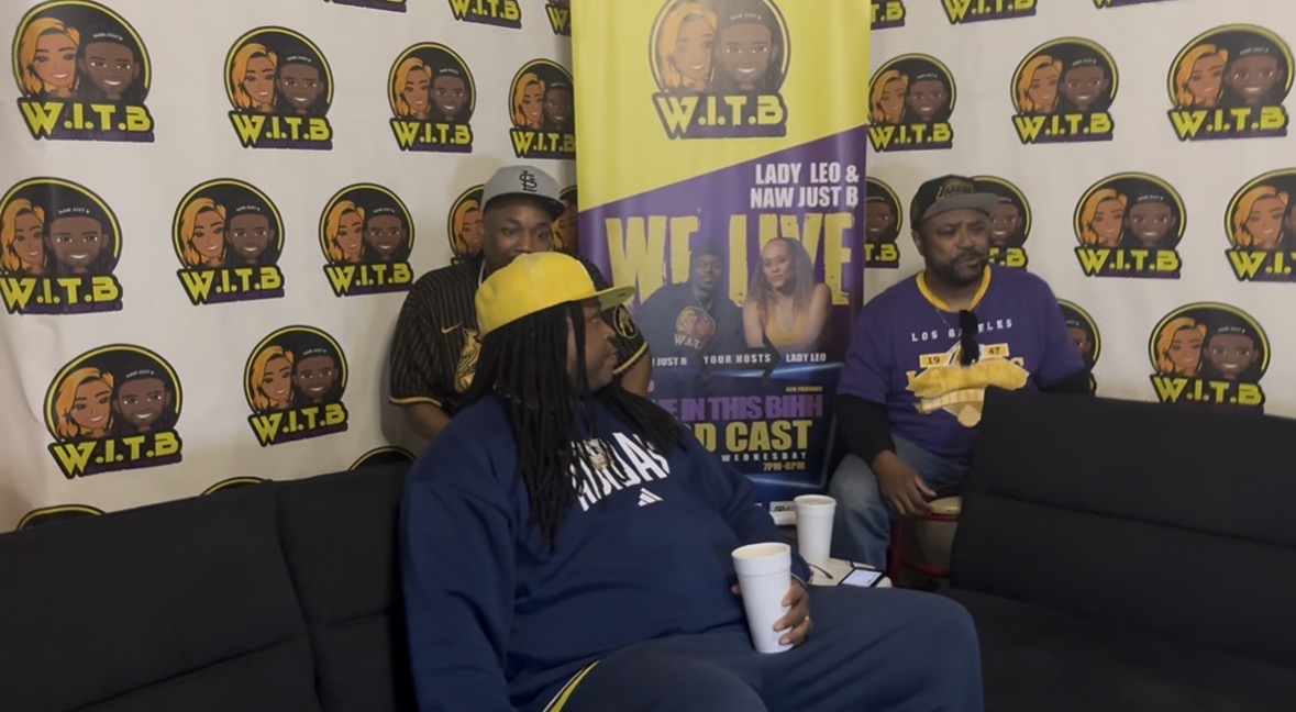 Three people sitting on a black couch in front of a W.I.T.B. branded backdrop, one holding a cup, one wearing a yellow hat.