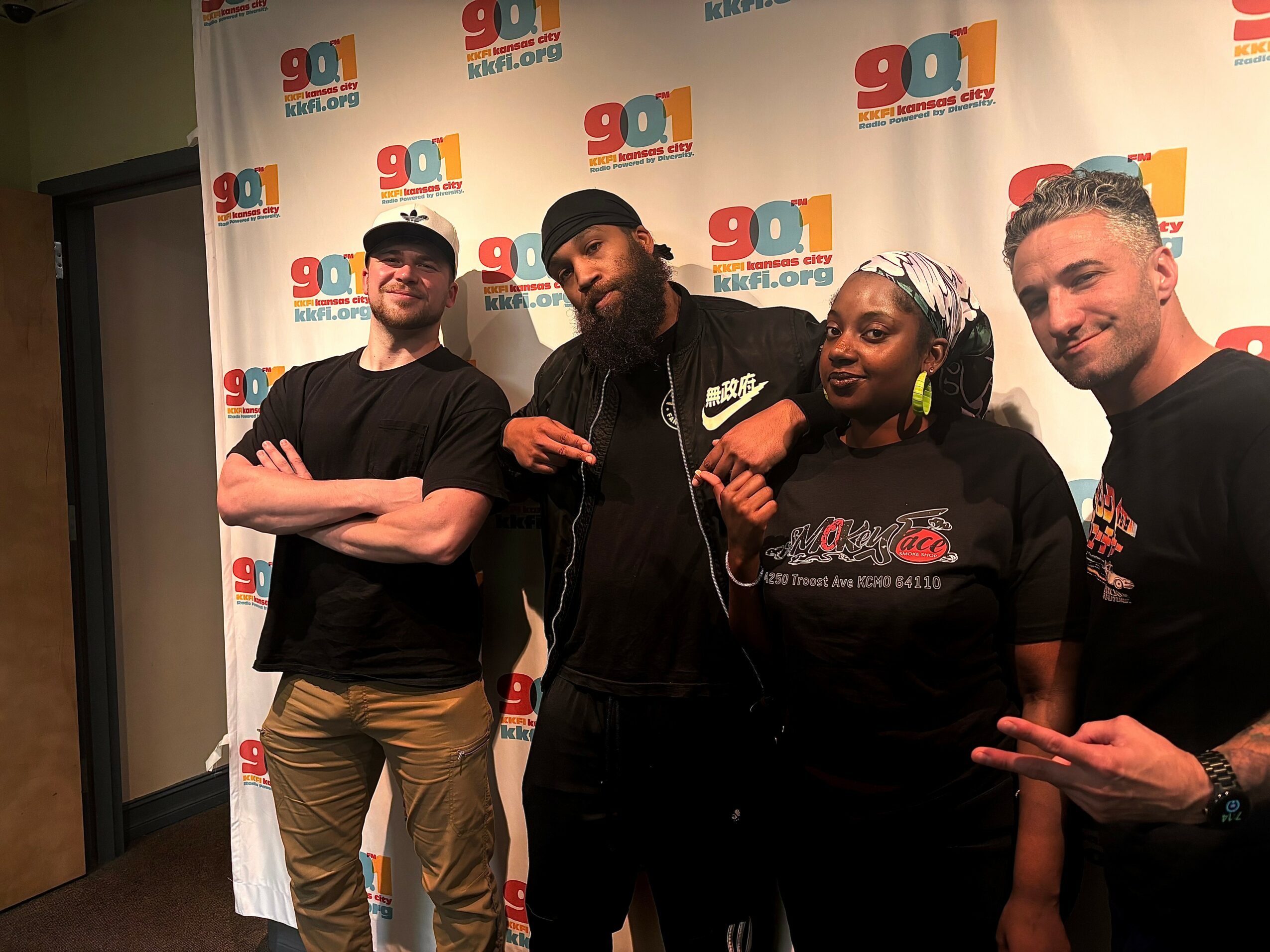 Four people standing in front of a backdrop with logos, smiling and posing for the camera.