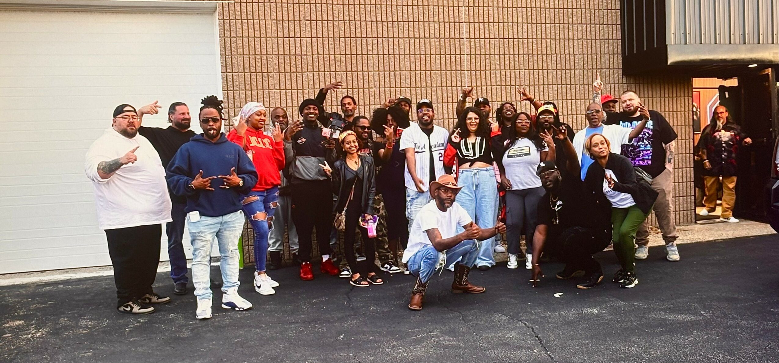 Group of people standing outside in front of a building, some smiling and posing for the photo.