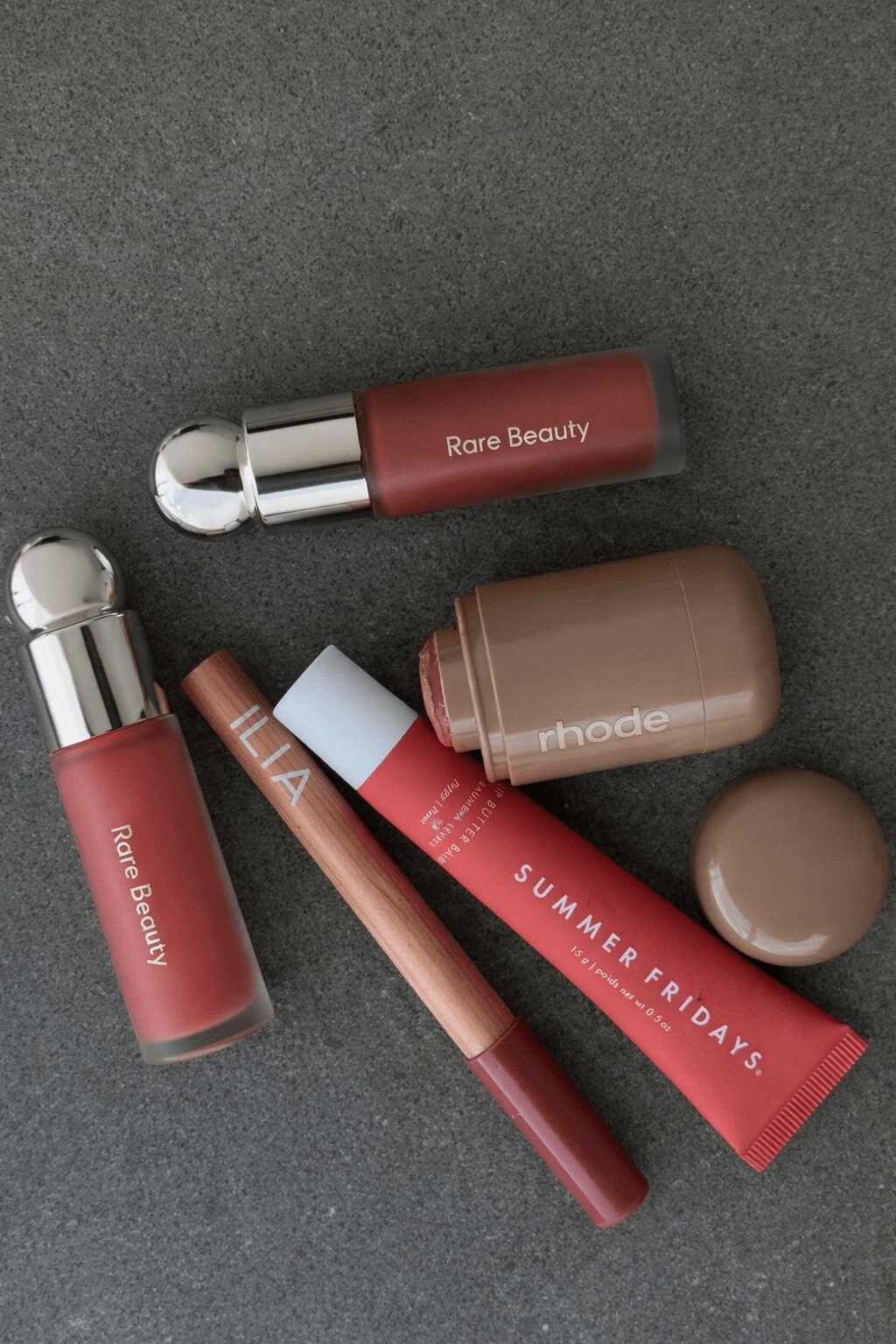 Various makeup and beauty products including lip gloss, lipstick, and a tube labeled 'SUMMER FASHION' on a dark surface.