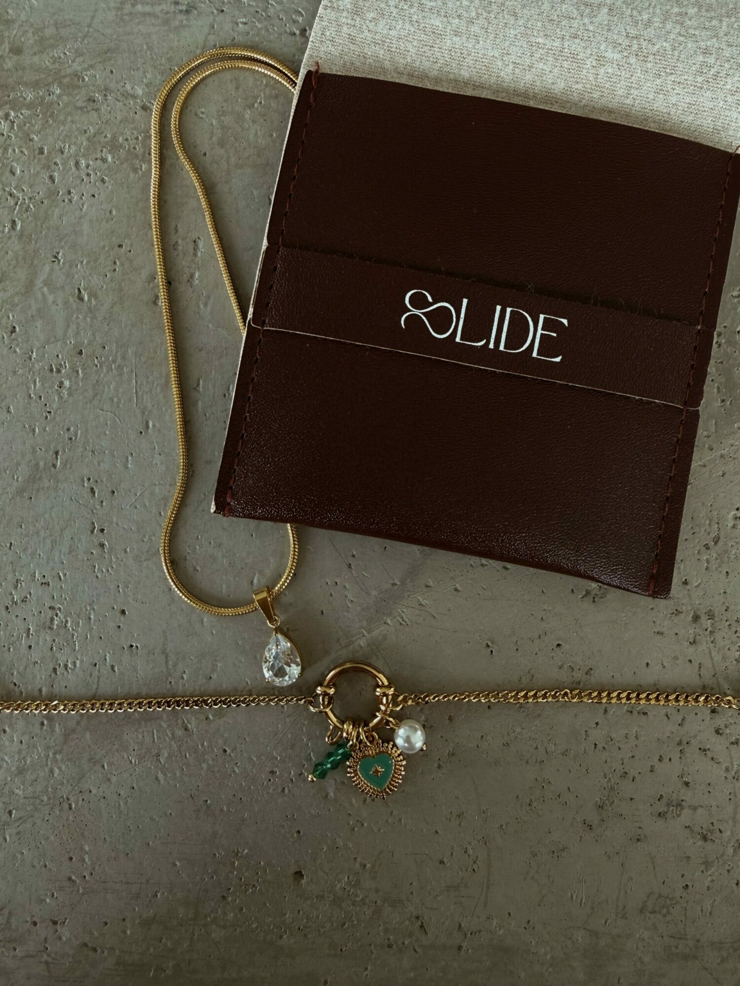 Brown cardholder with white text, gold chain with charms, on gray surface.