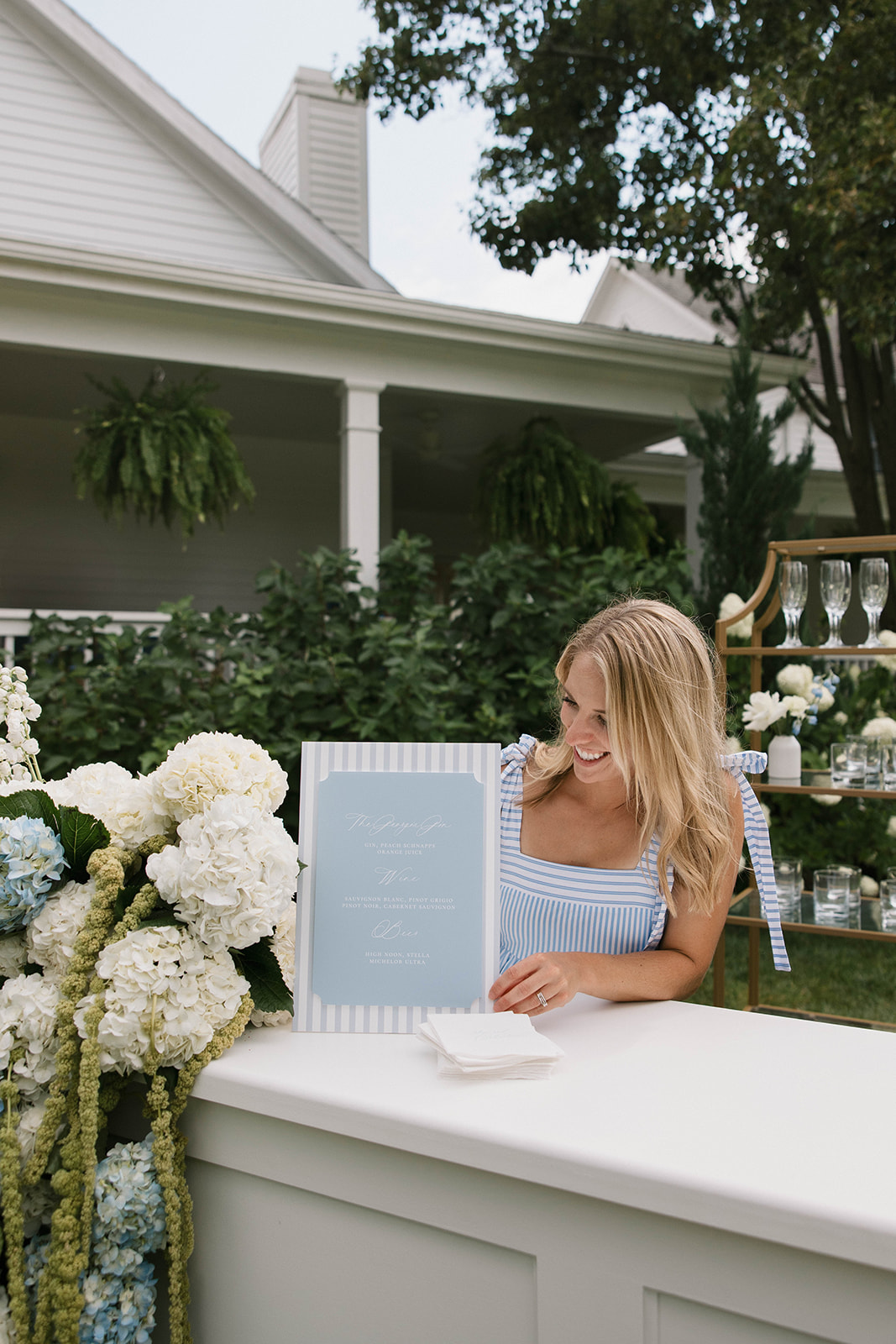 Woman with long blonde hair reading a menu outdoors, surrounded by white flowers and greenery.