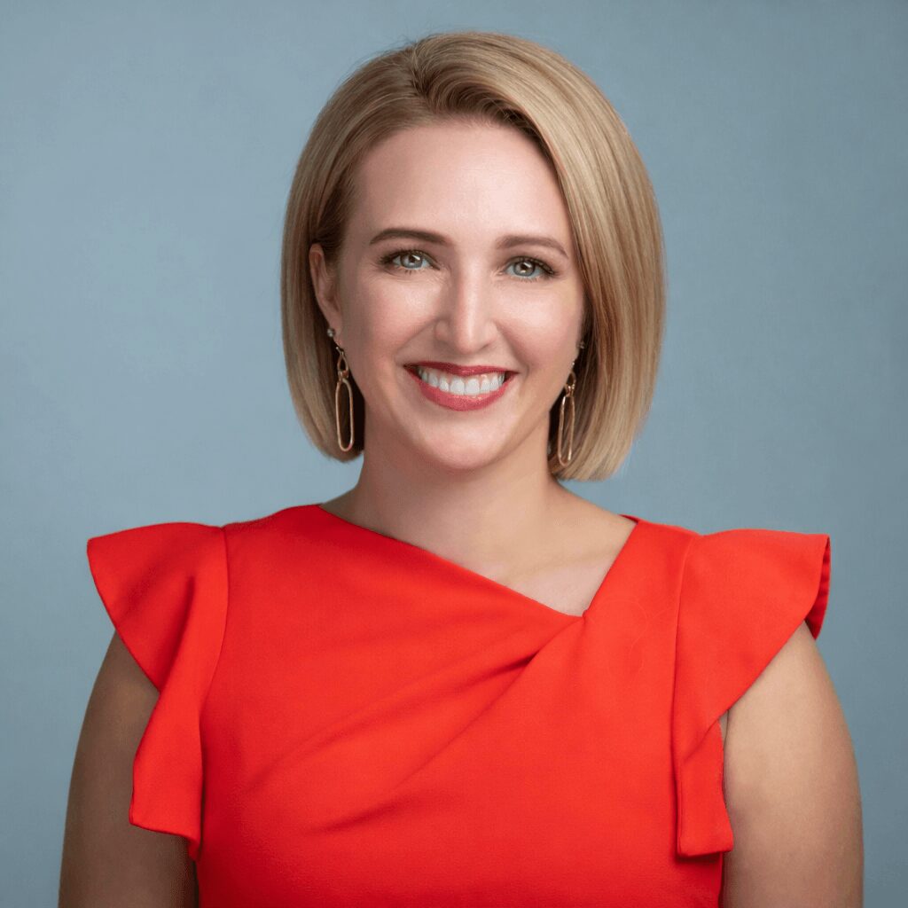 Smiling woman with blonde hair in a red dress against a blue background.