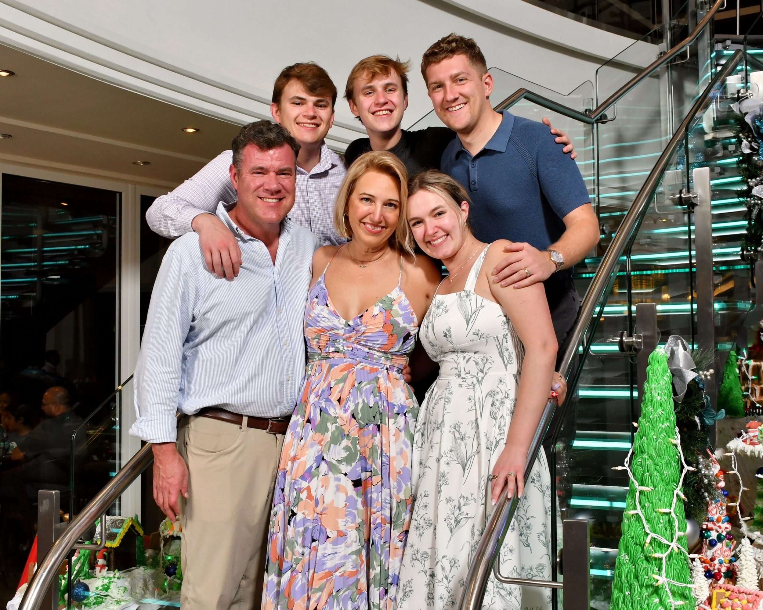 Group of six people smiling on a staircase at an indoor event, with a glass railing and decorations nearby.
