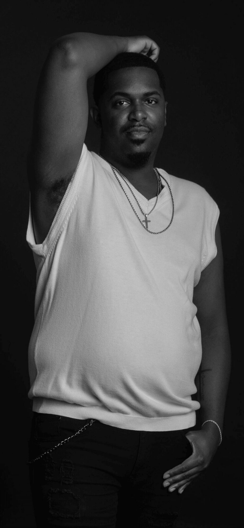 Person with arm raised, wearing a sleeveless top and necklace, looking at the camera, in black and white.