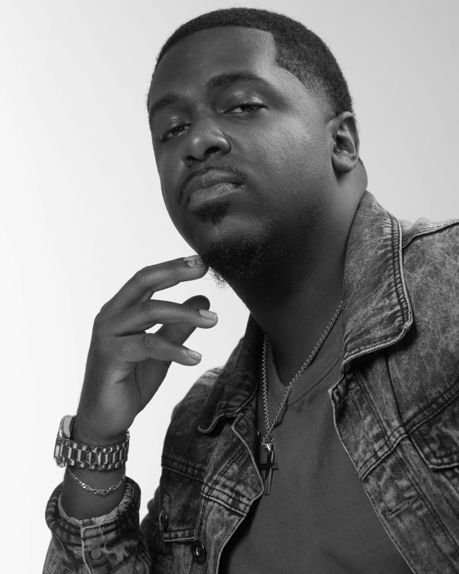 Black and white portrait of a man with short hair, wearing a denim jacket and a watch, looking confidently at the camera.