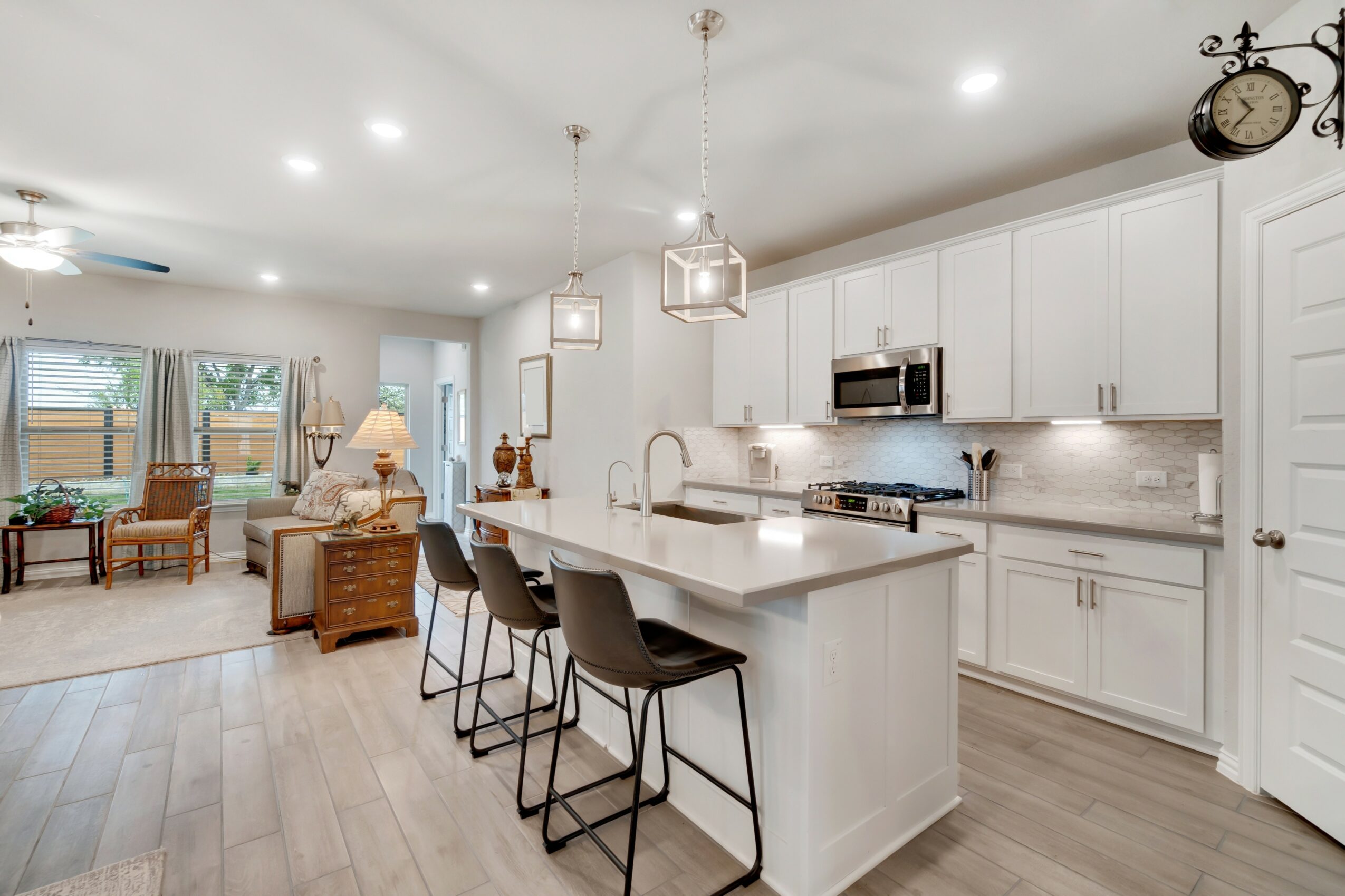 Open-concept kitchen and living room with white cabinets, island, bar stools, and seating area, bright and modern interior.