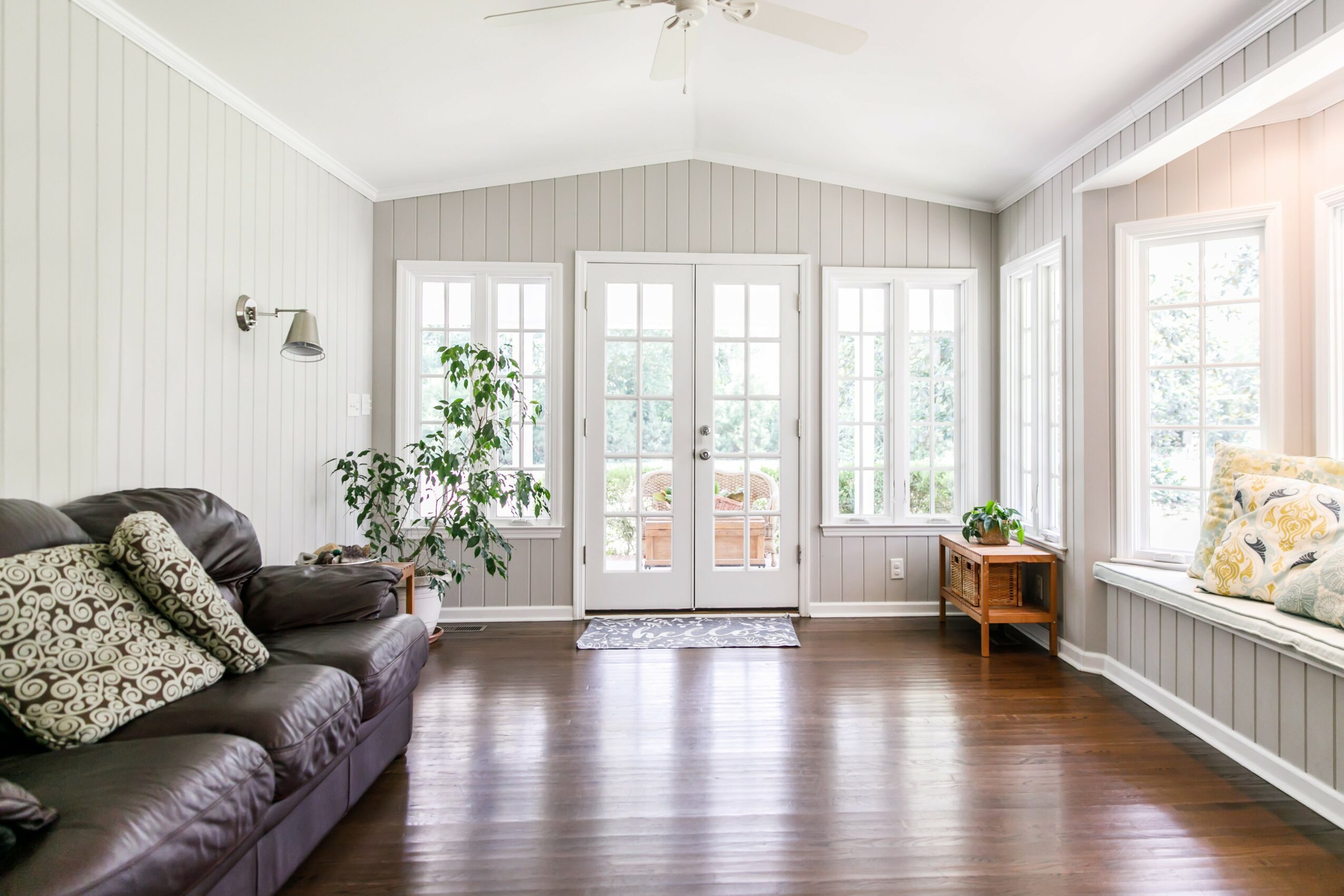 Living room with large windows, a dark leather sofa, a potted plant, and a small side table, bright and airy.