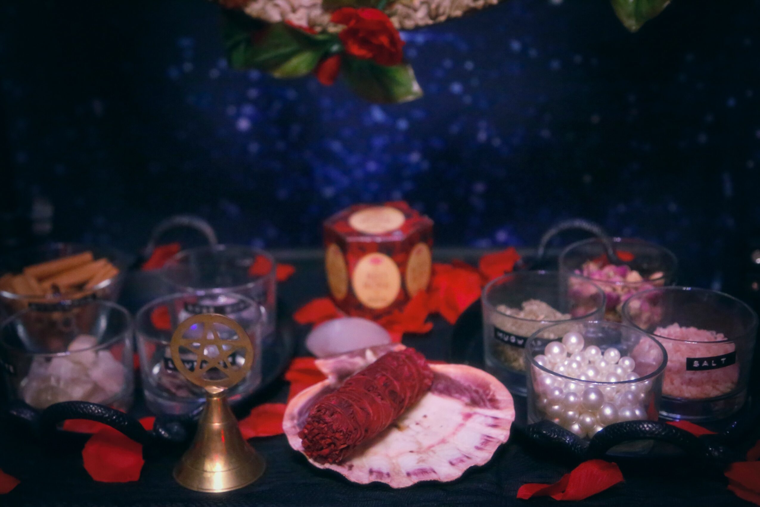 Decorative table with candles, shells, and jewelry against a starry background, with red flower petals scattered around.