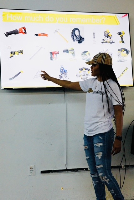 Girl with long hair, wearing a striped cap and white shirt, points at a presentation screen displaying various tools.