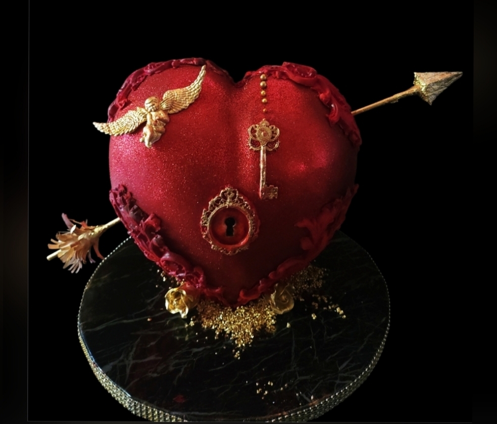 Red heart-shaped object with gold and silver decorative elements, including an arrow piercing it, on a black background.