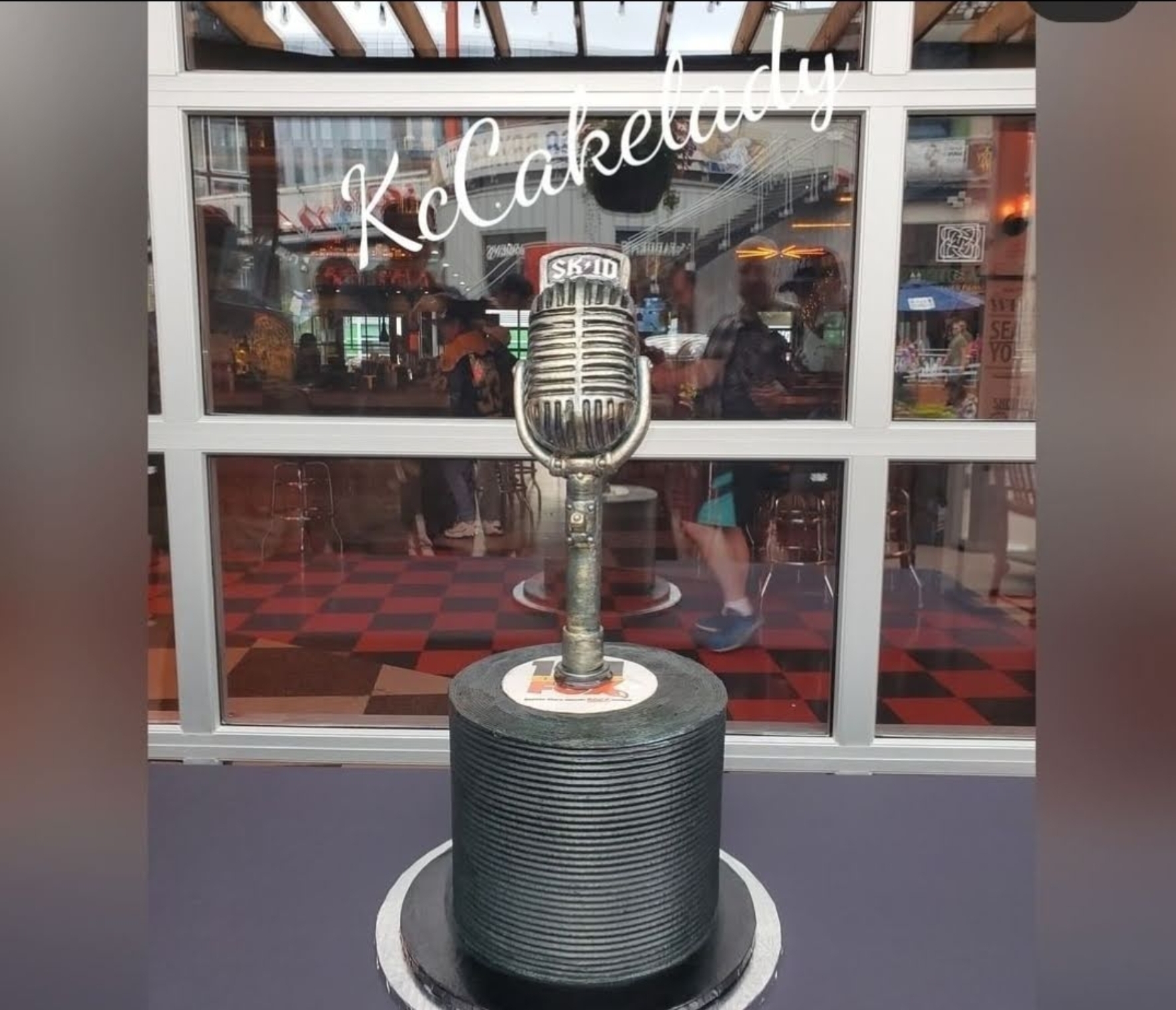 A trophy shaped like a microphone on a black cylindrical base, with a sign reading 'K-Calendar' above, in front of a window.