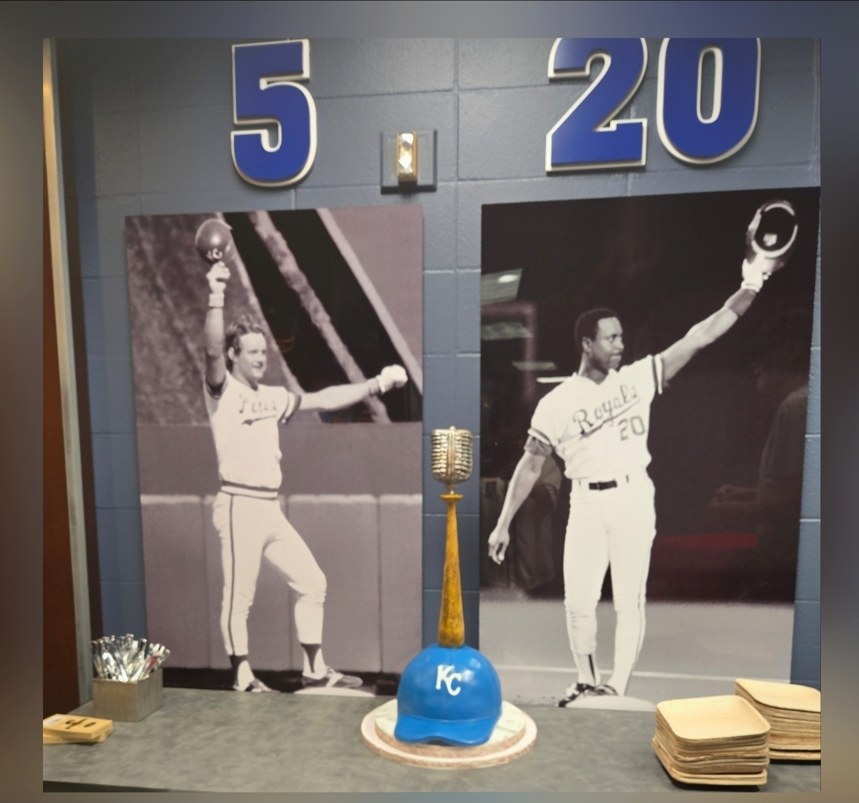 Two black and white photos of a baseball player holding a bat and a ball, with large numbers 5 and 20 above, and a blue Kansas City Royals cap in front.
