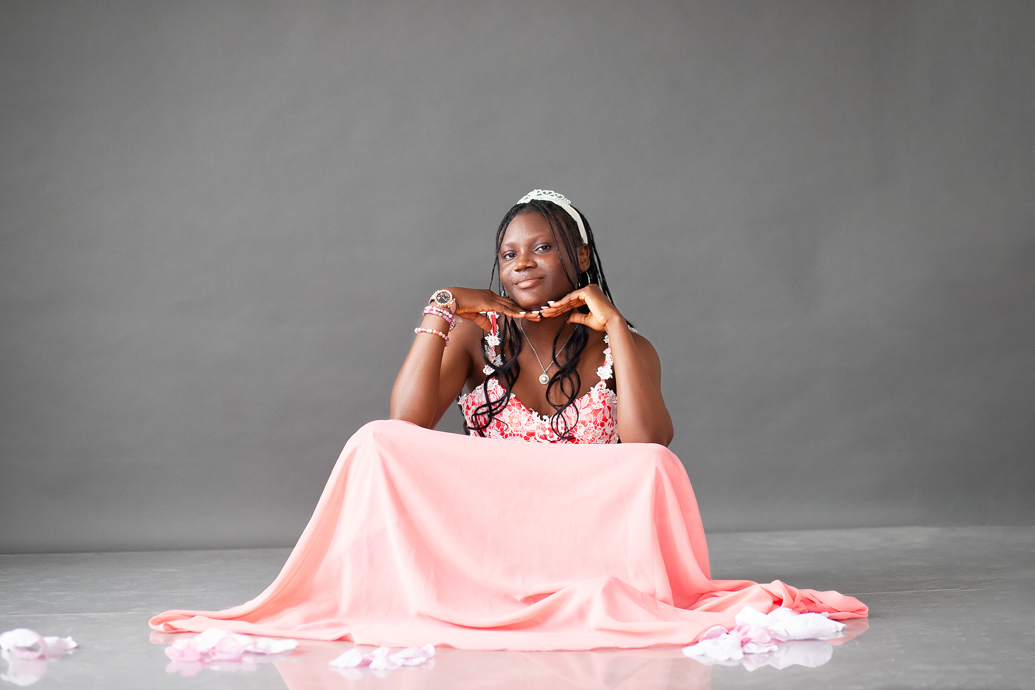 Young girl with headphones sitting at a table covered with a pink cloth, smiling, against a gray background.