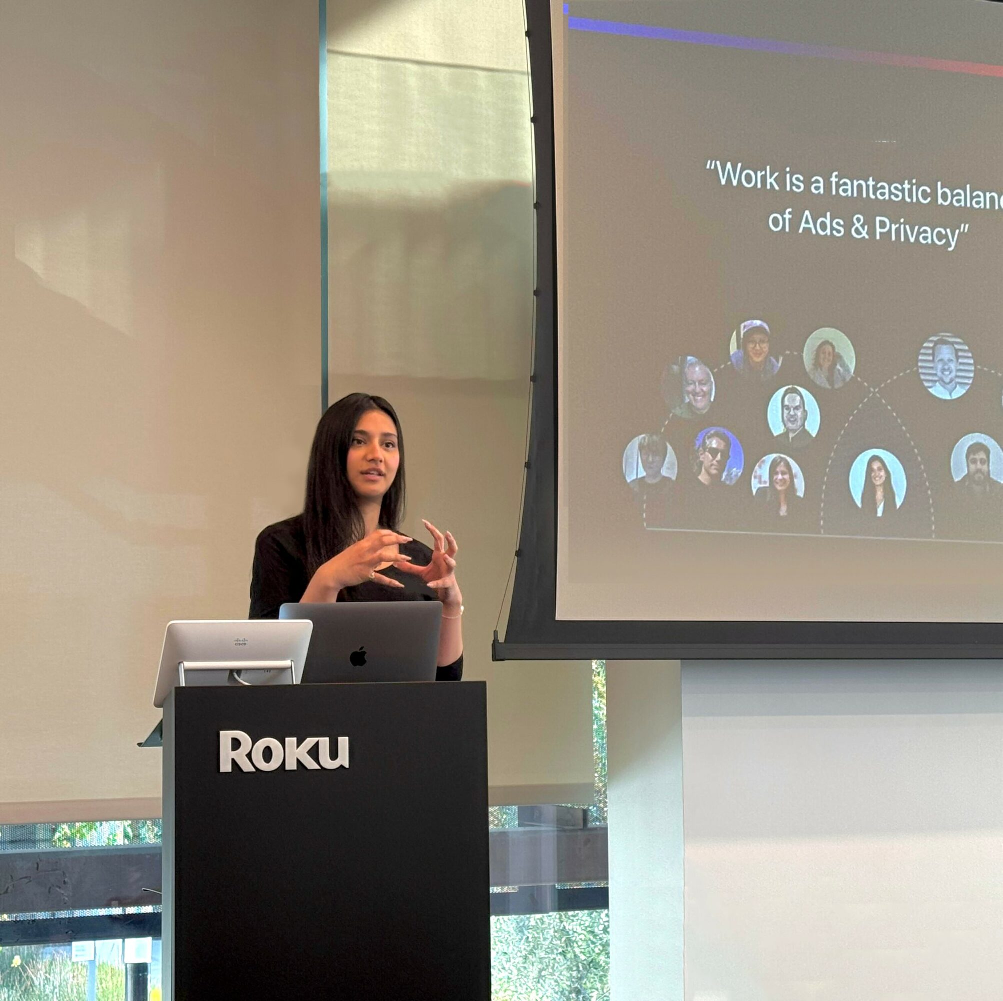 Woman giving a presentation in front of a screen with a quote and circular images, standing behind a Roku podium.
