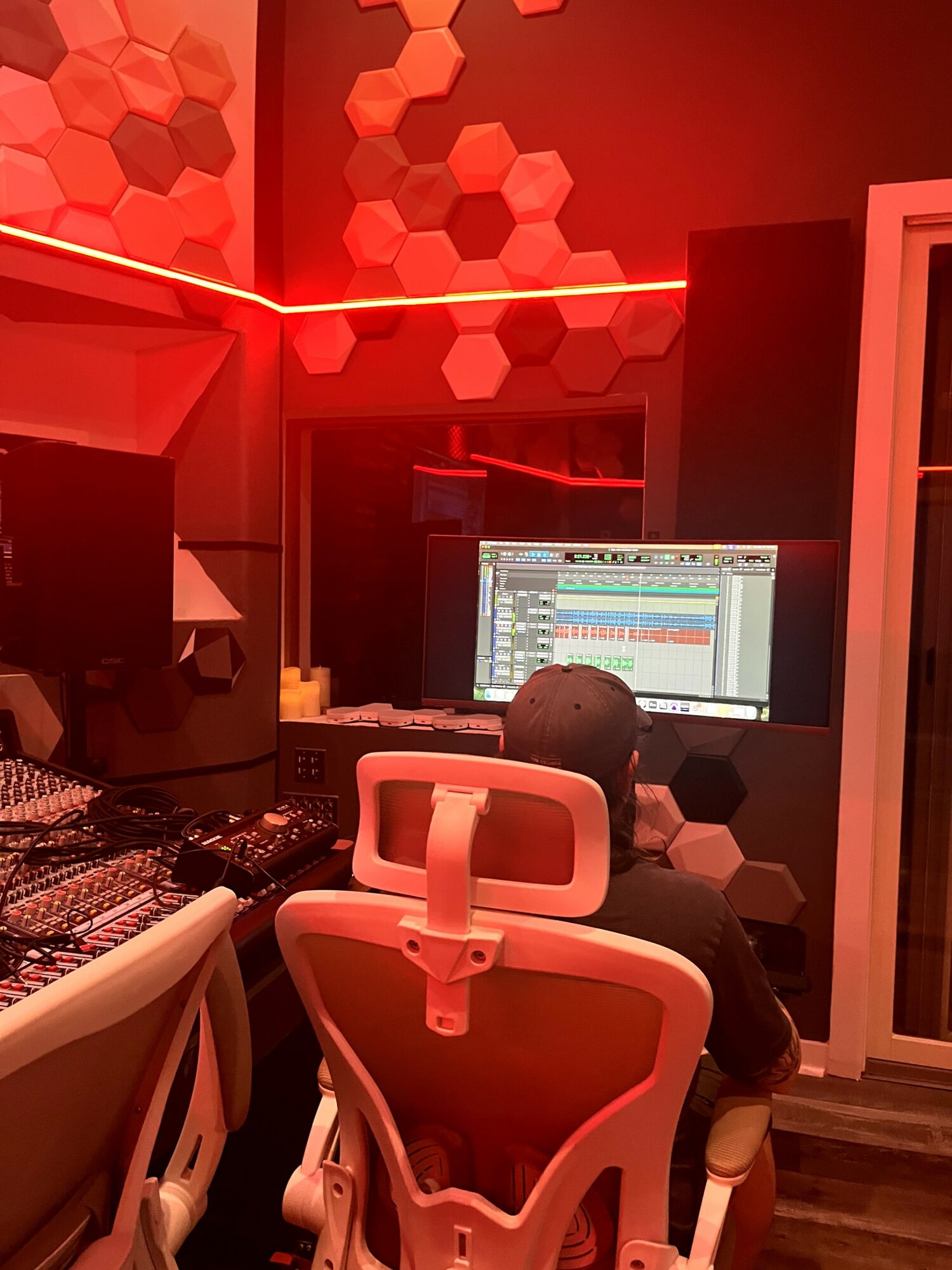 Person working at a computer in a music studio with red lighting and hexagonal wall decorations.