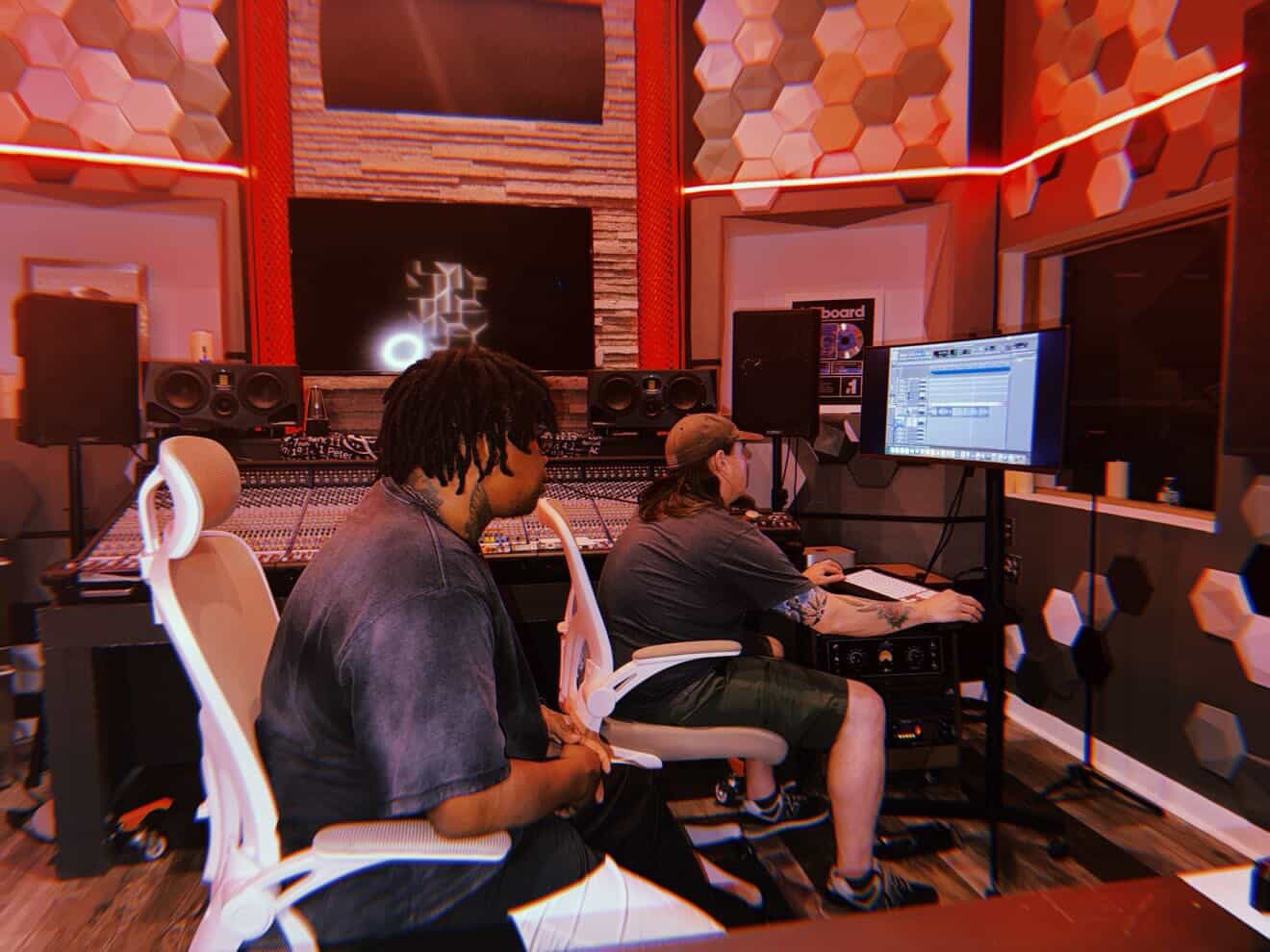 Two people working at computers in a colorful recording studio with sound equipment and monitors.