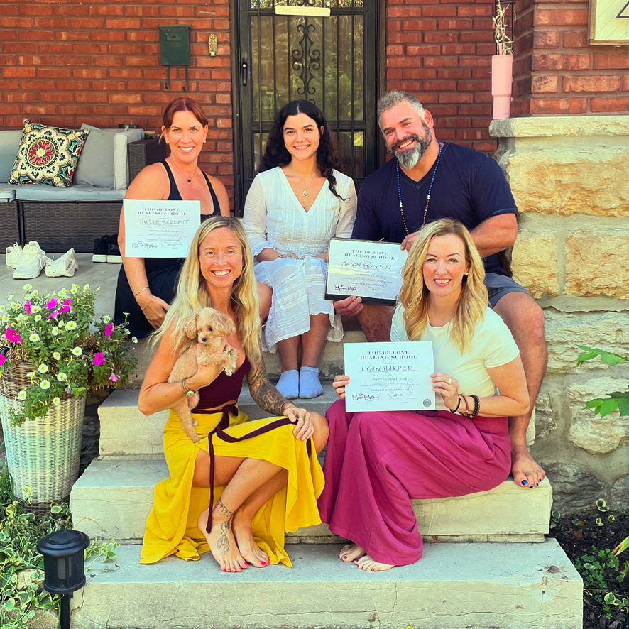 Group of five people, three women and two men, sitting and standing on steps outside a brick house, holding certificates.