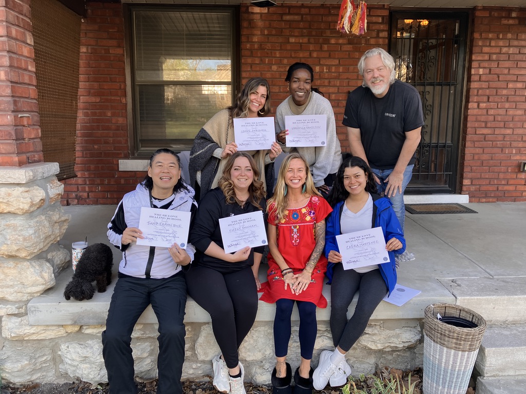 Six people, five women and one man, holding certificates, standing on a porch in front of a brick house, smiling.