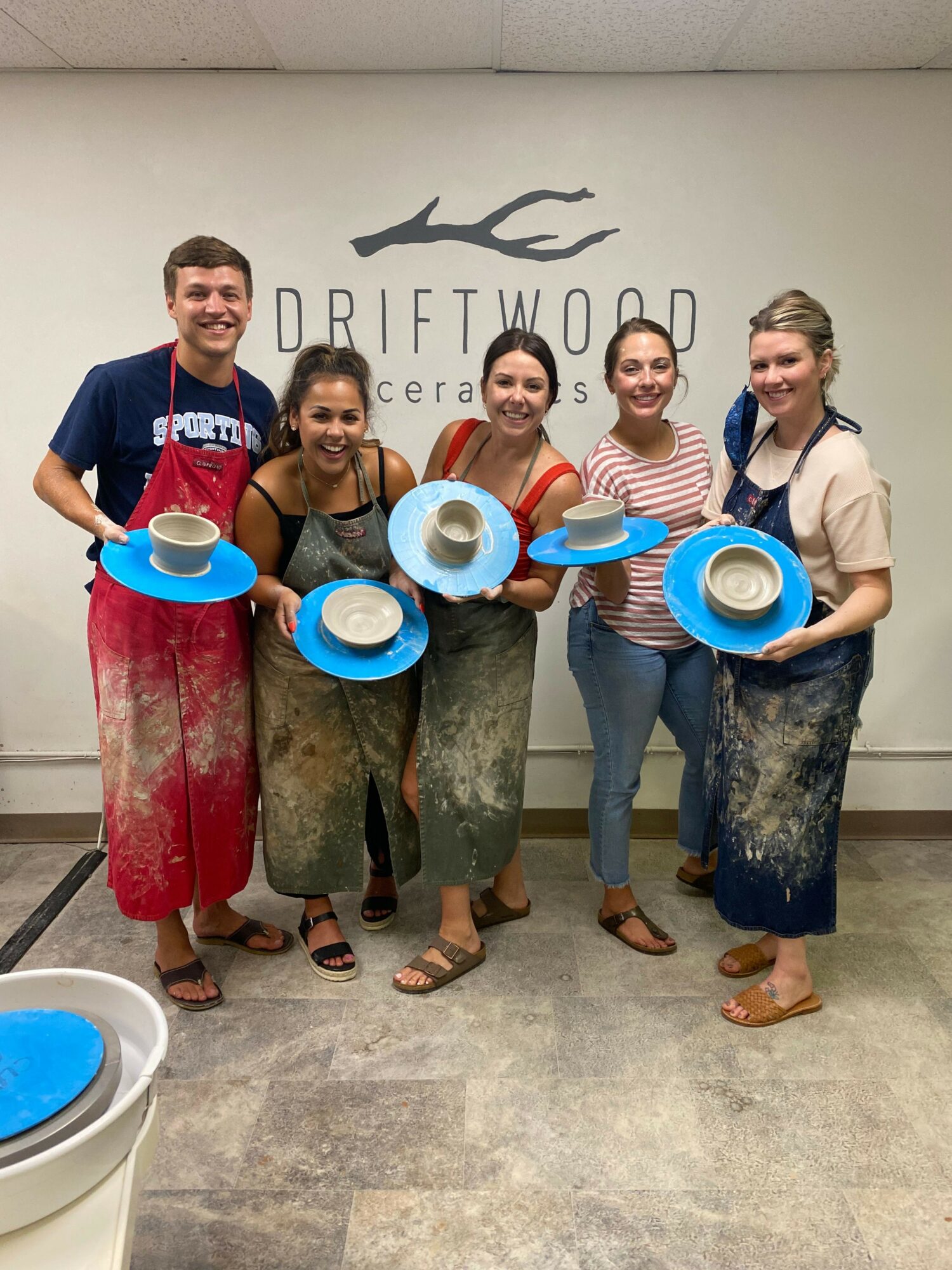 Four women standing indoors, holding blue and white plates, smiling, with a sign reading 'DIPLOMACY' in the background.