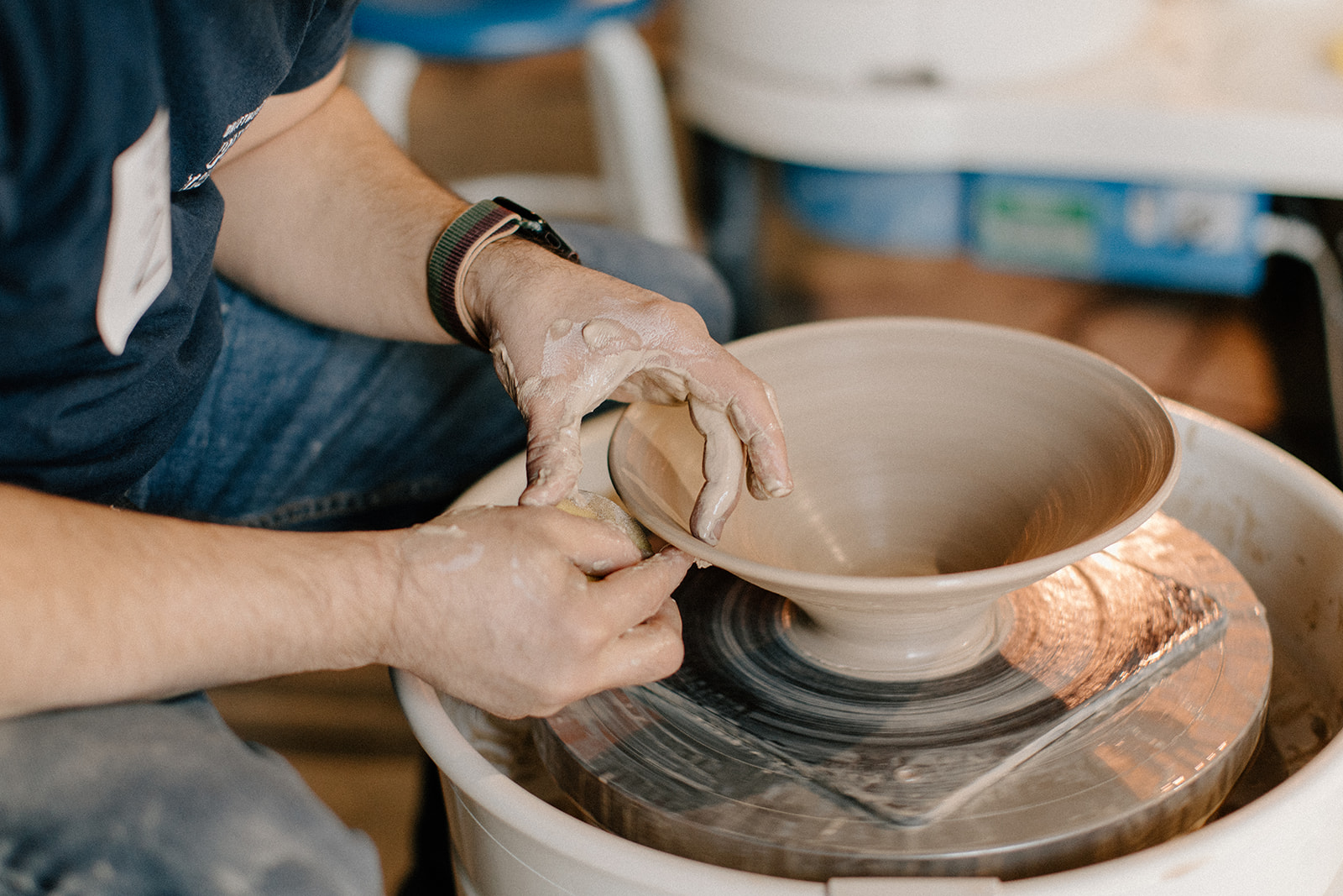 Person shaping clay on pottery wheel with hands, pottery in progress, workshop background, neutral lighting.