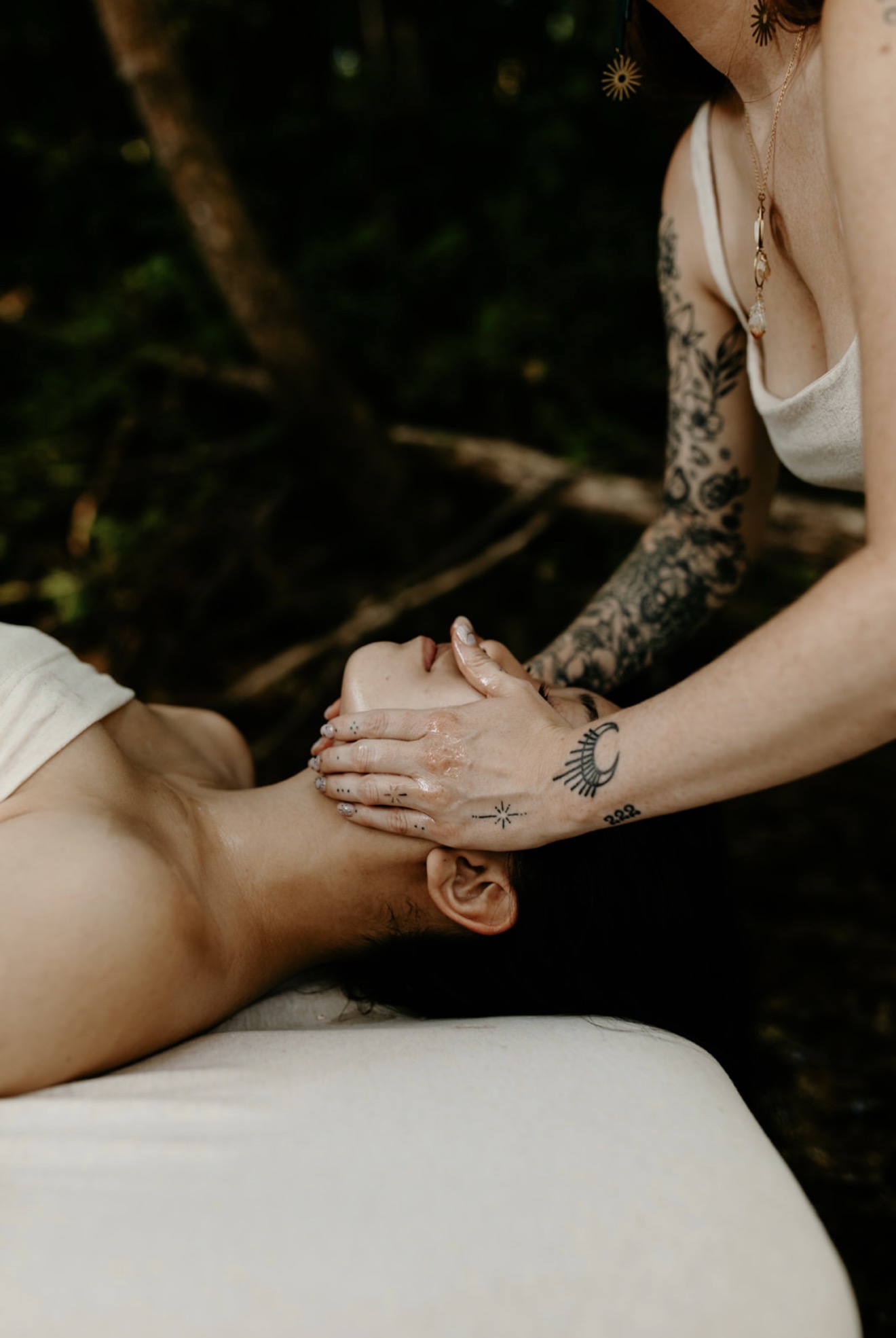 Person receiving a massage outdoors, lying face up with hands on their face, surrounded by greenery.