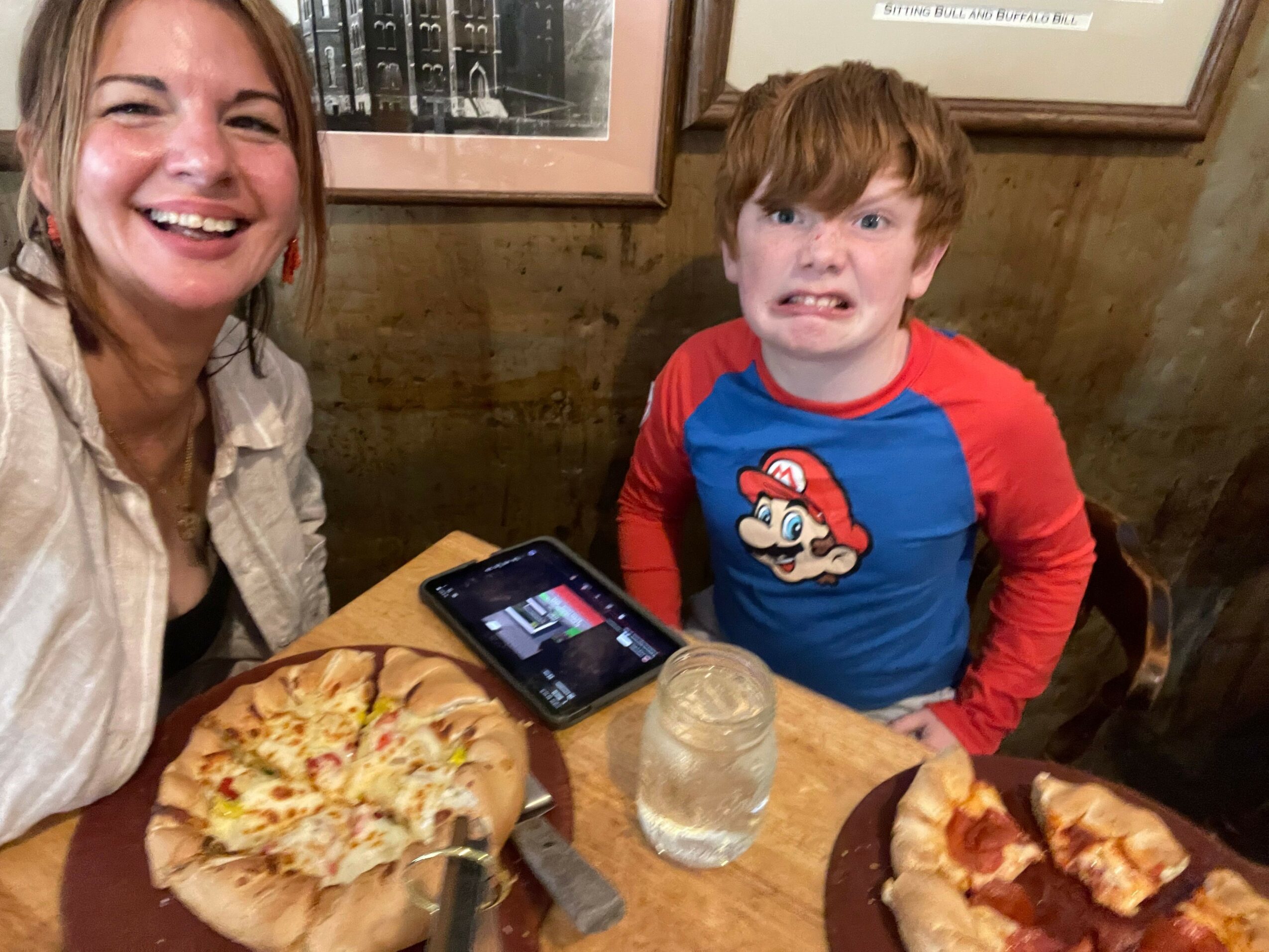 Child and adult smiling at a table with pizza, drinks, and a phone, viewed from above.