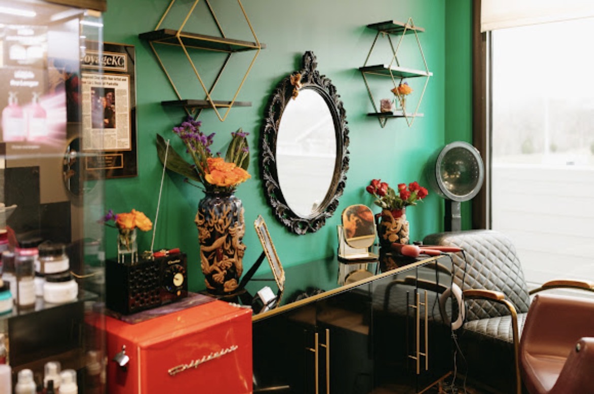 Interior with green wall, mirror, shelves, flowers, and seating area, near a window with sunlight.