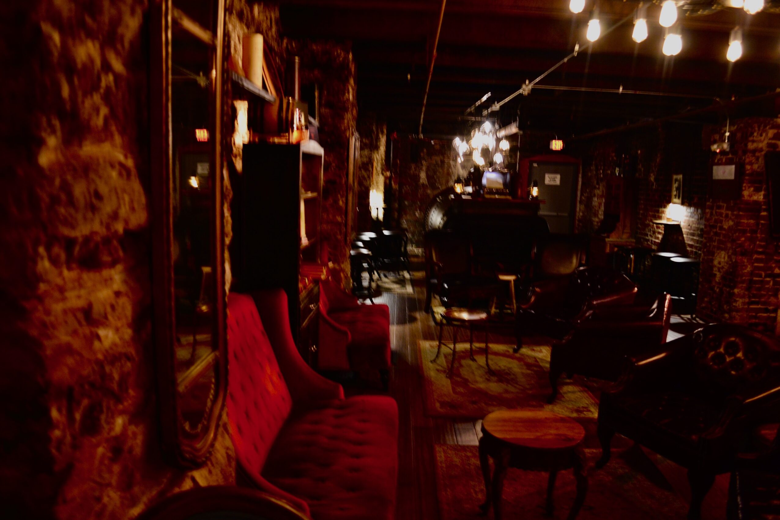 Interior of a dimly lit room with red chairs, wooden shelves, and warm lighting, creating a cozy atmosphere.