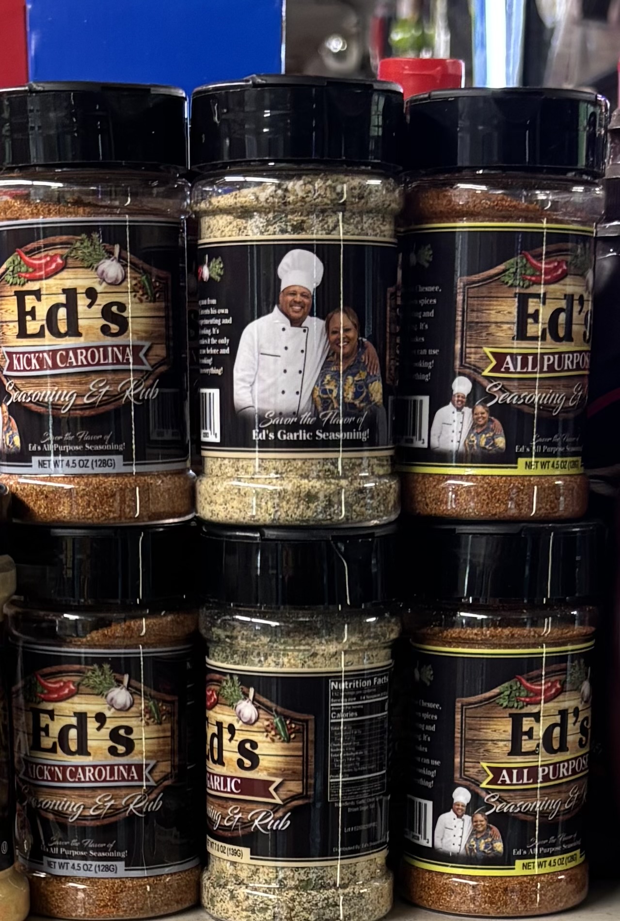 Three spice jars with labels, one jar with a chef's photo, arranged on a surface. The jars contain various spices.