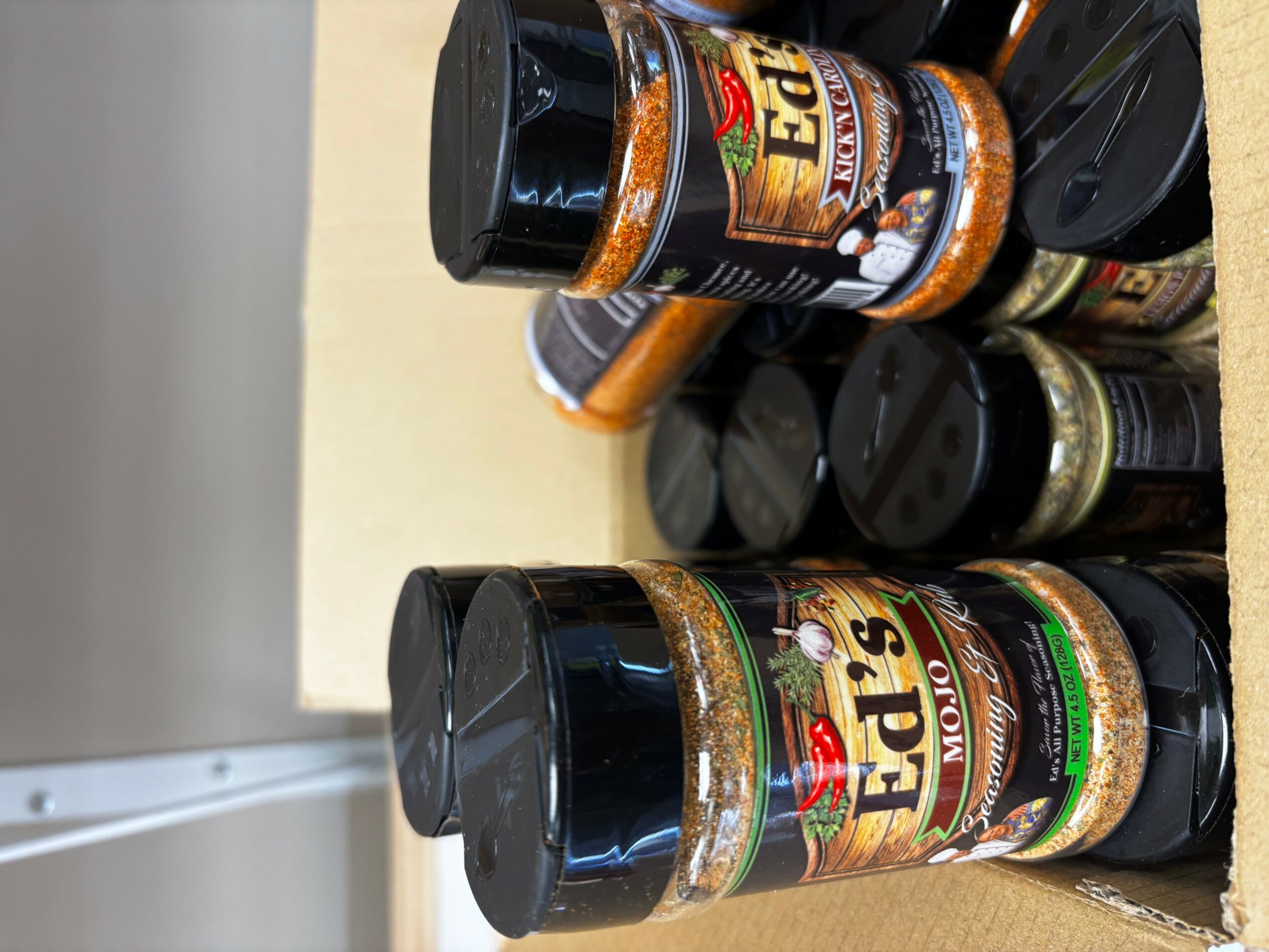 Several jars of Ed's seasoning spices stacked on a shelf, with black lids and colorful labels.