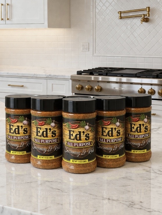 Six jars of Ed's All Purpose seasoning on a kitchen countertop, with a stove and white tiled wall in the background.