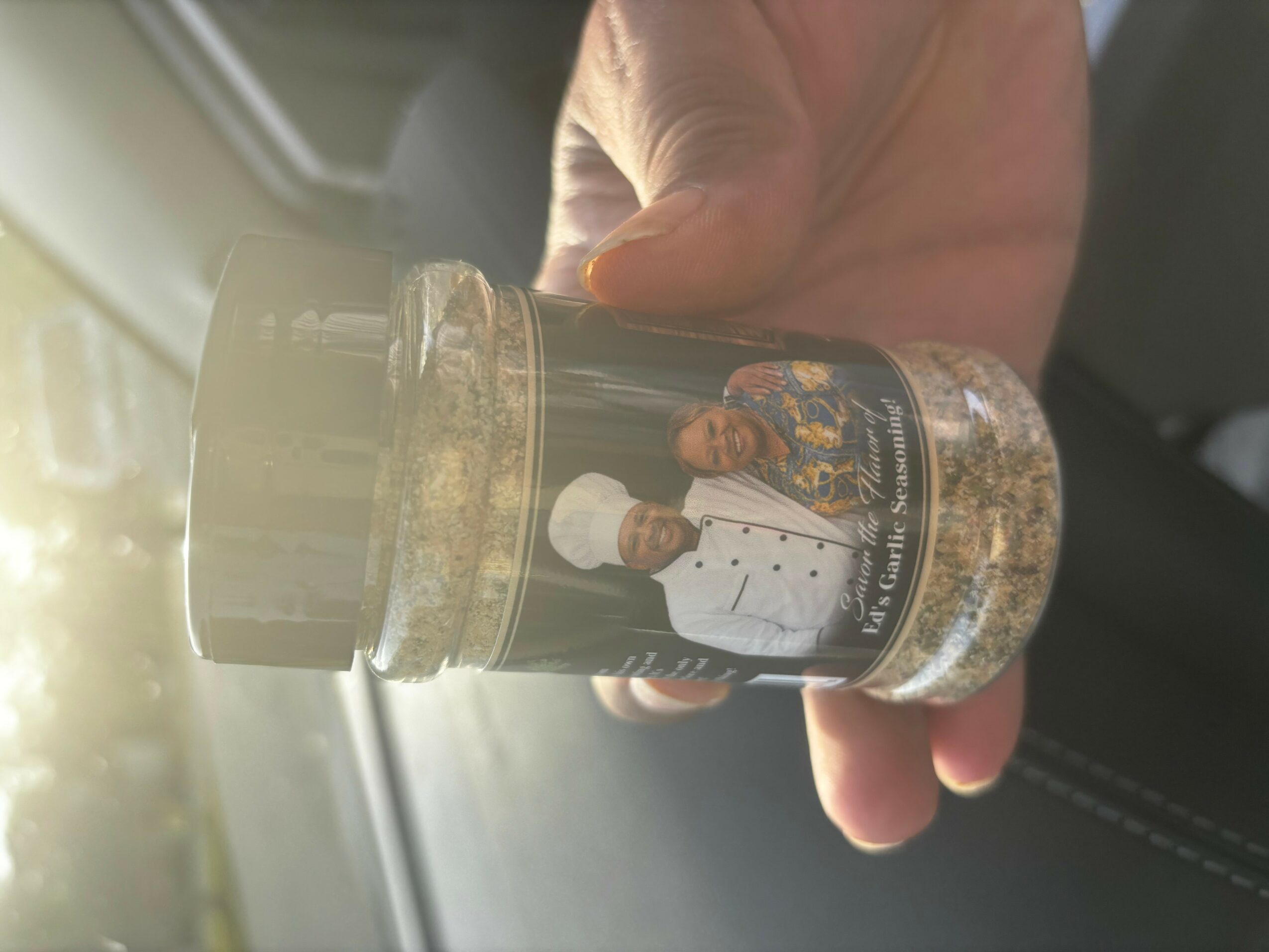 Hand holding a jar with a label showing a chef in a white uniform and hat, and food inside the jar.