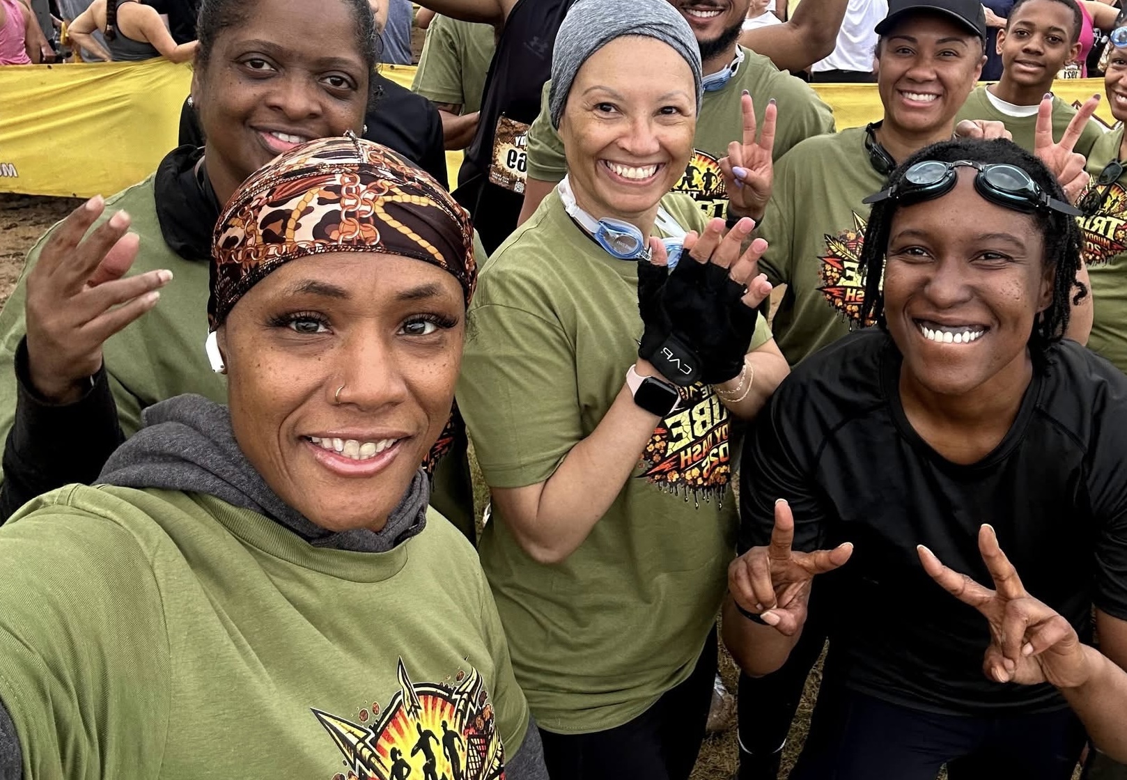 Group of smiling women outdoors, some making peace signs, wearing casual clothing and head coverings.