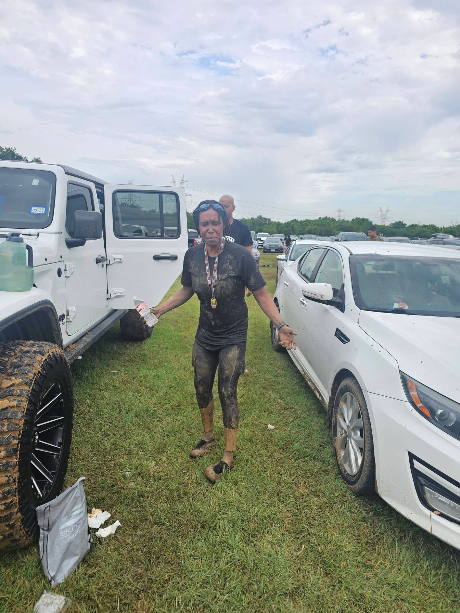 Person walking on grass between parked vehicles, cloudy sky above.