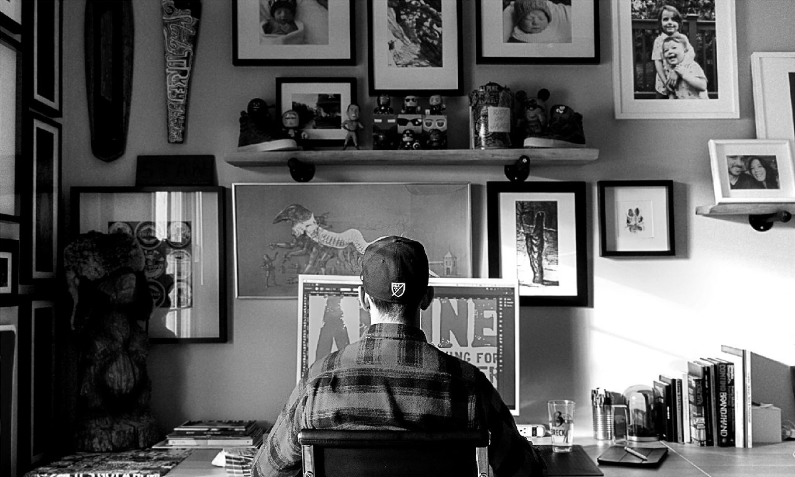 Person sitting at desk in front of a wall with multiple framed pictures and shelves.