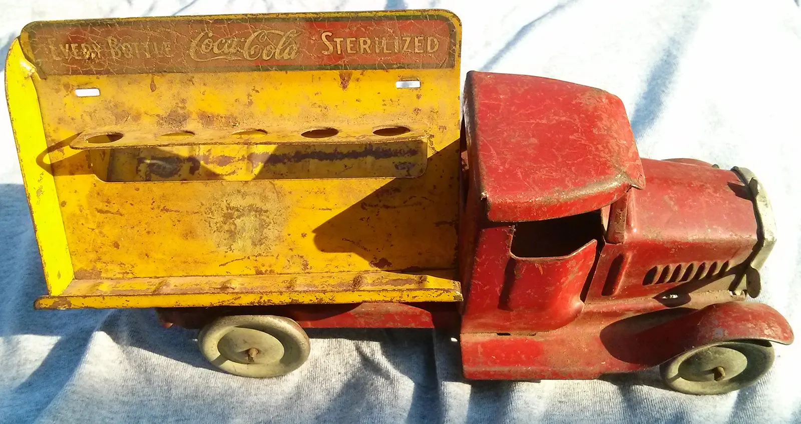 Old Coca-Cola toy truck with a yellow back and red front, showing signs of wear and dirt.