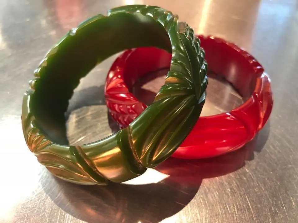 Two plastic bangles, one green and one red, placed on a reflective surface with a blurred background.