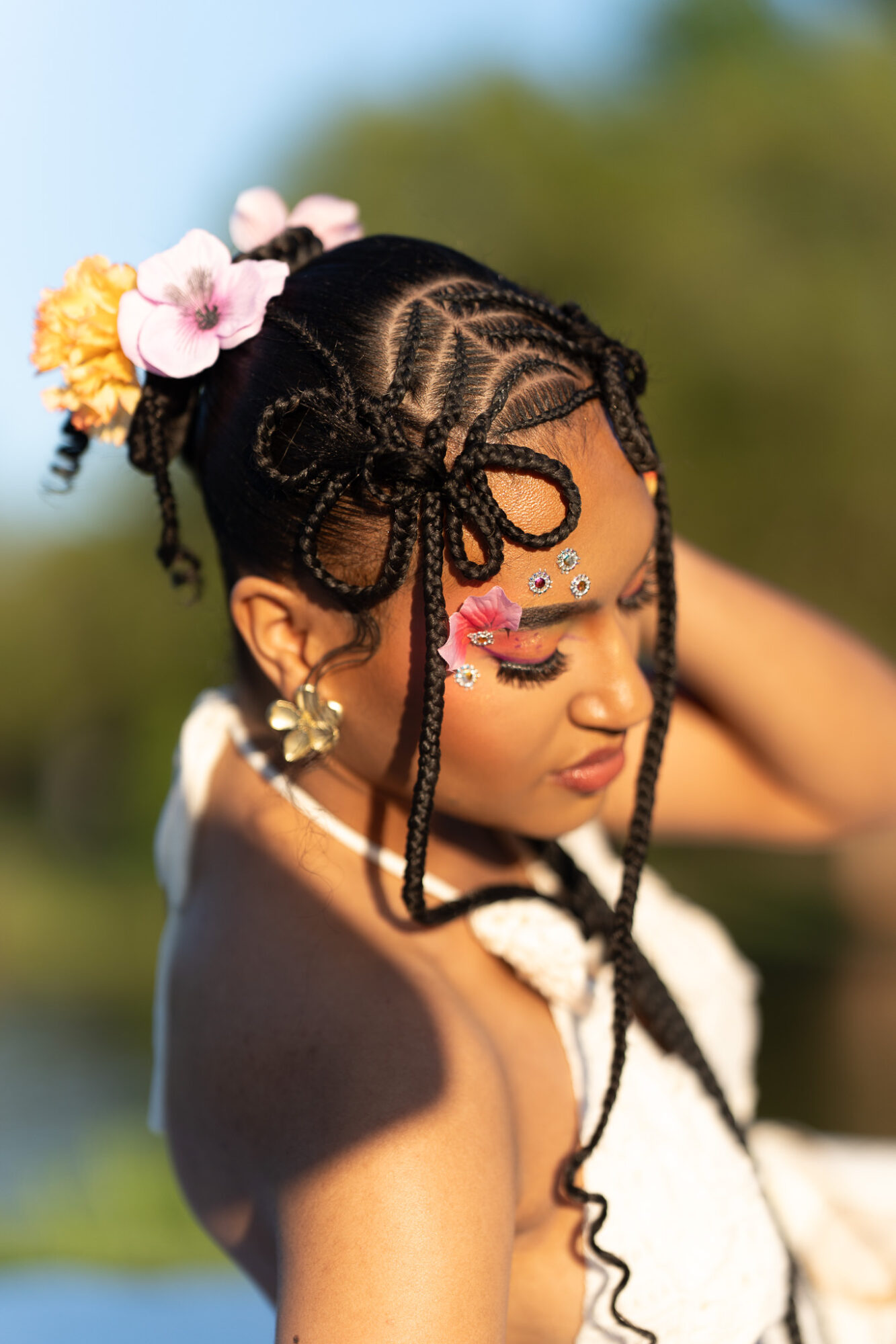 Young girl with braided hairstyle decorated with flowers and jewelry, outdoors with blurred green background.