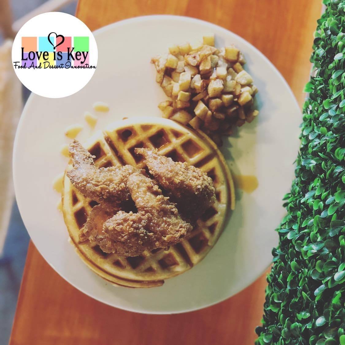 Plate with fried chicken, waffle, and potato salad on a table, with a green plant on the side.