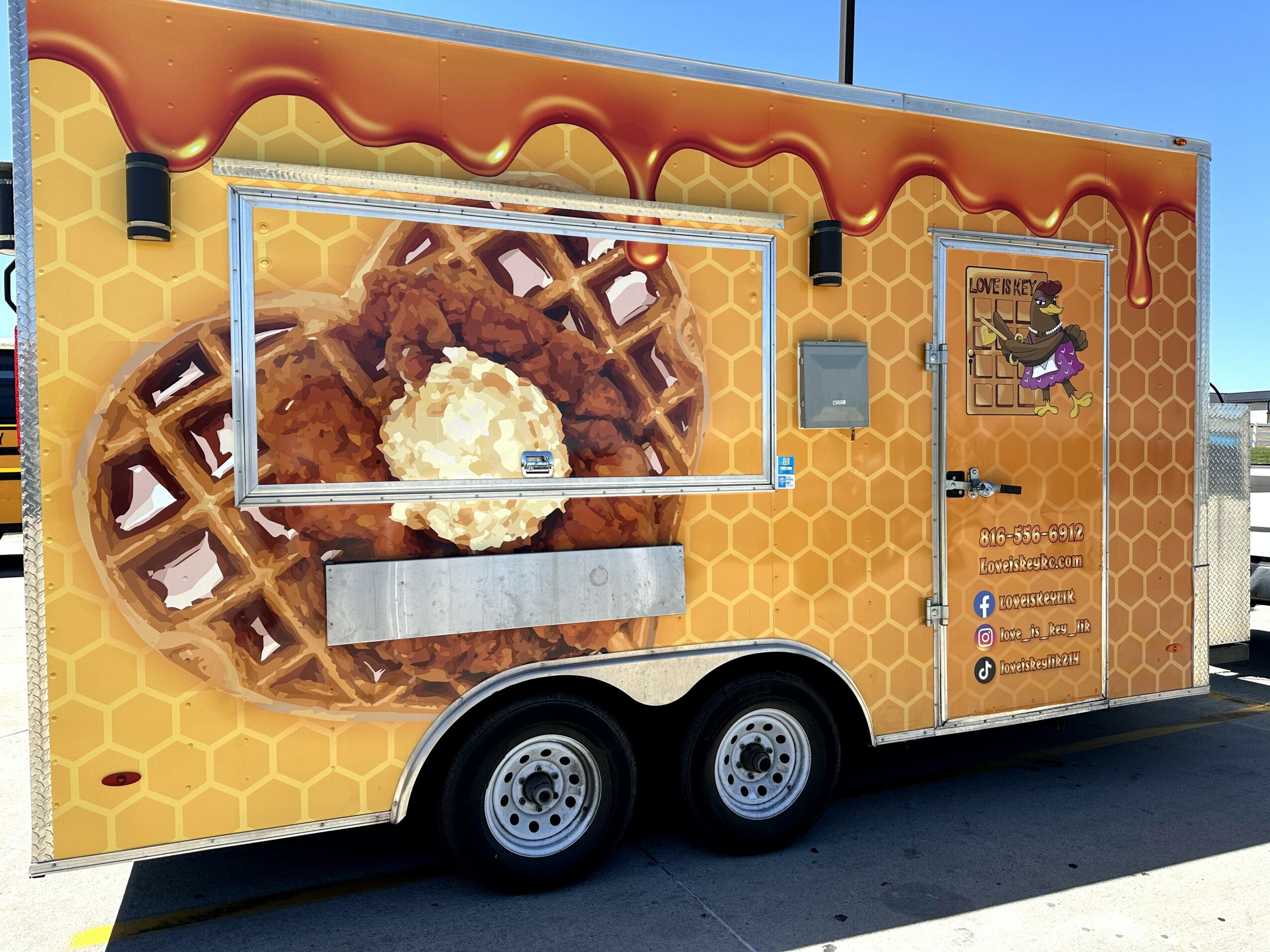 Food truck decorated with honeycomb and waffle images, featuring a window with a waffle and ice cream, and a door with a cartoon bee.