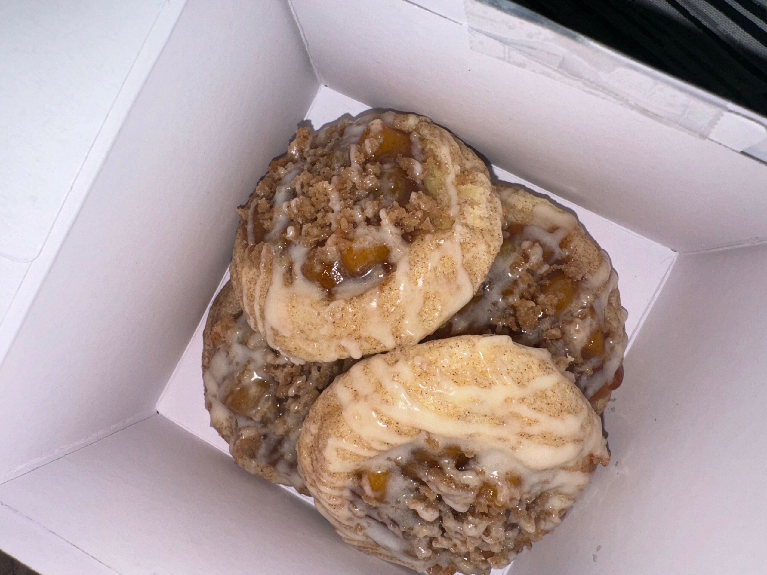 Three cookies with toppings inside a white box, one with caramel and nuts, others with icing and toppings.