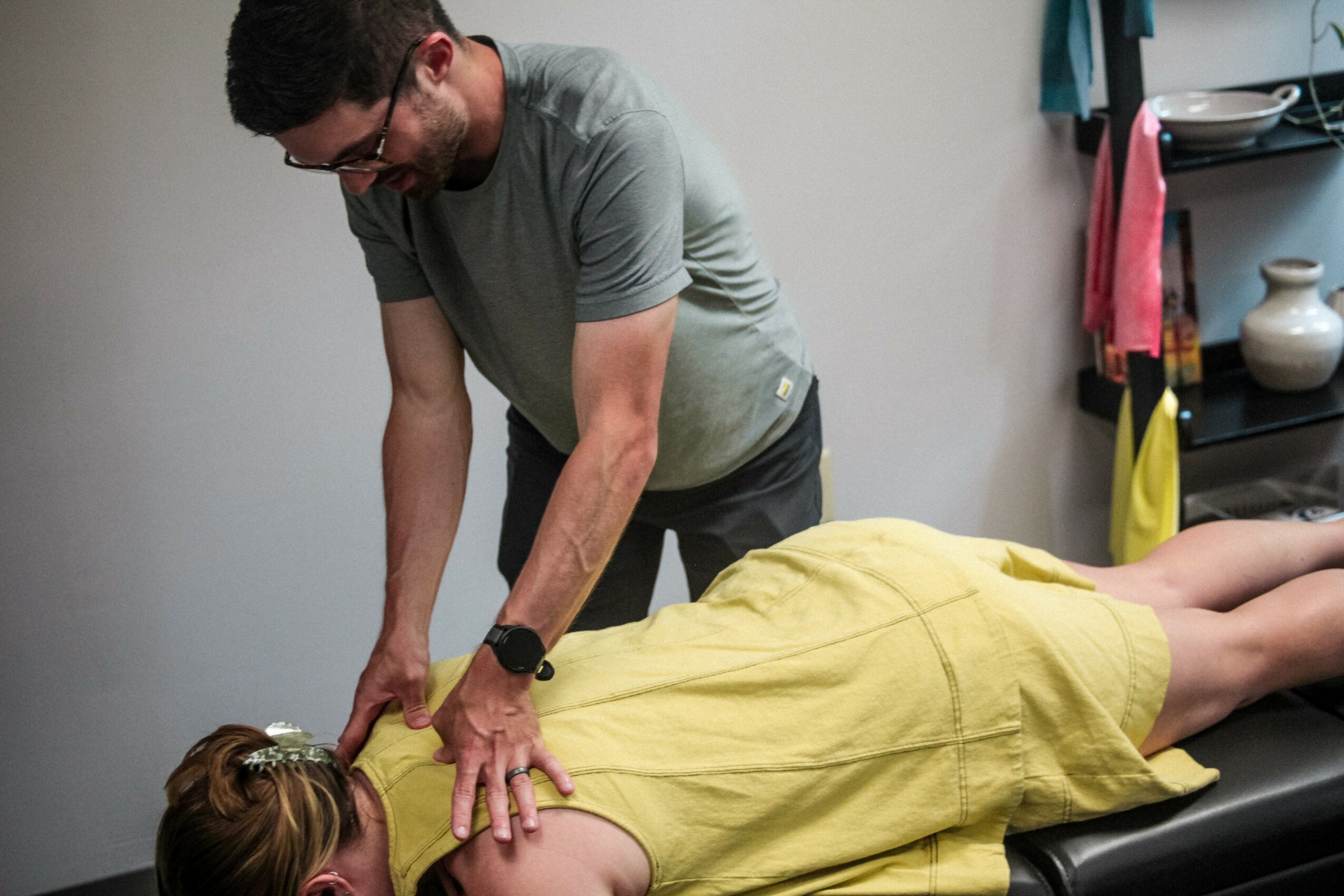 A person lying face down on a massage table, covered with a yellow towel, receiving a massage from a therapist.