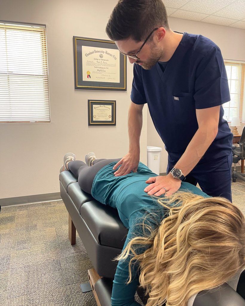Healthcare professional performs a physical exam on a patient lying face down on an examination table in a clinic room.