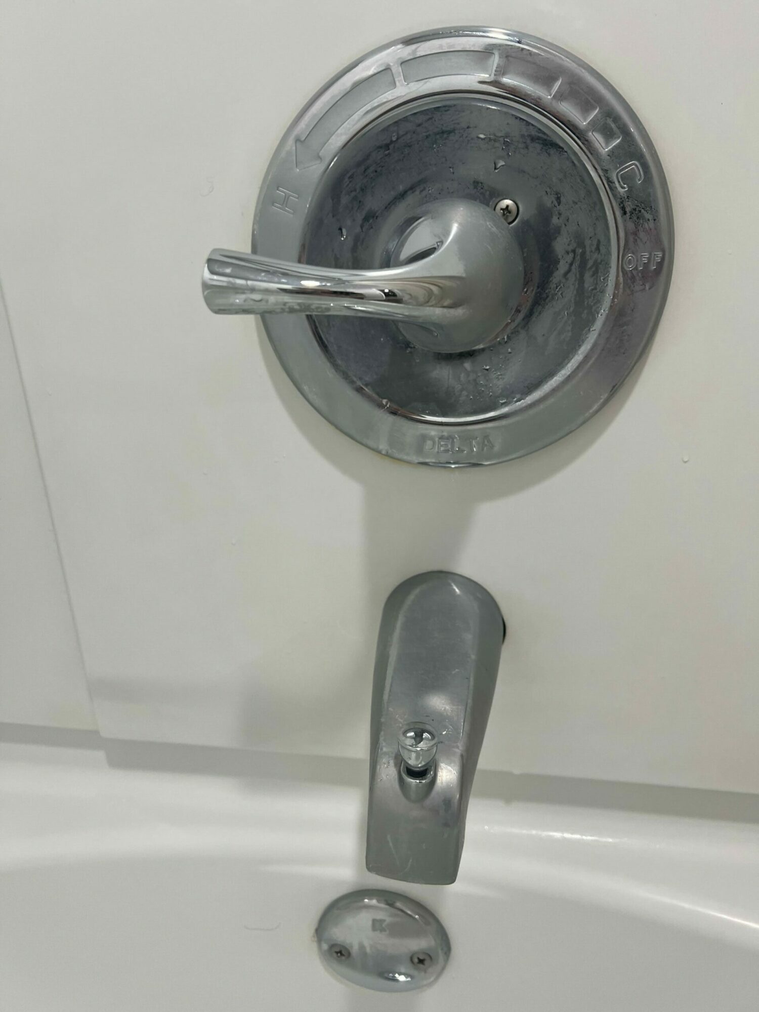 Close-up of a silver faucet handle, a metal latch, and a small round object on a white surface.